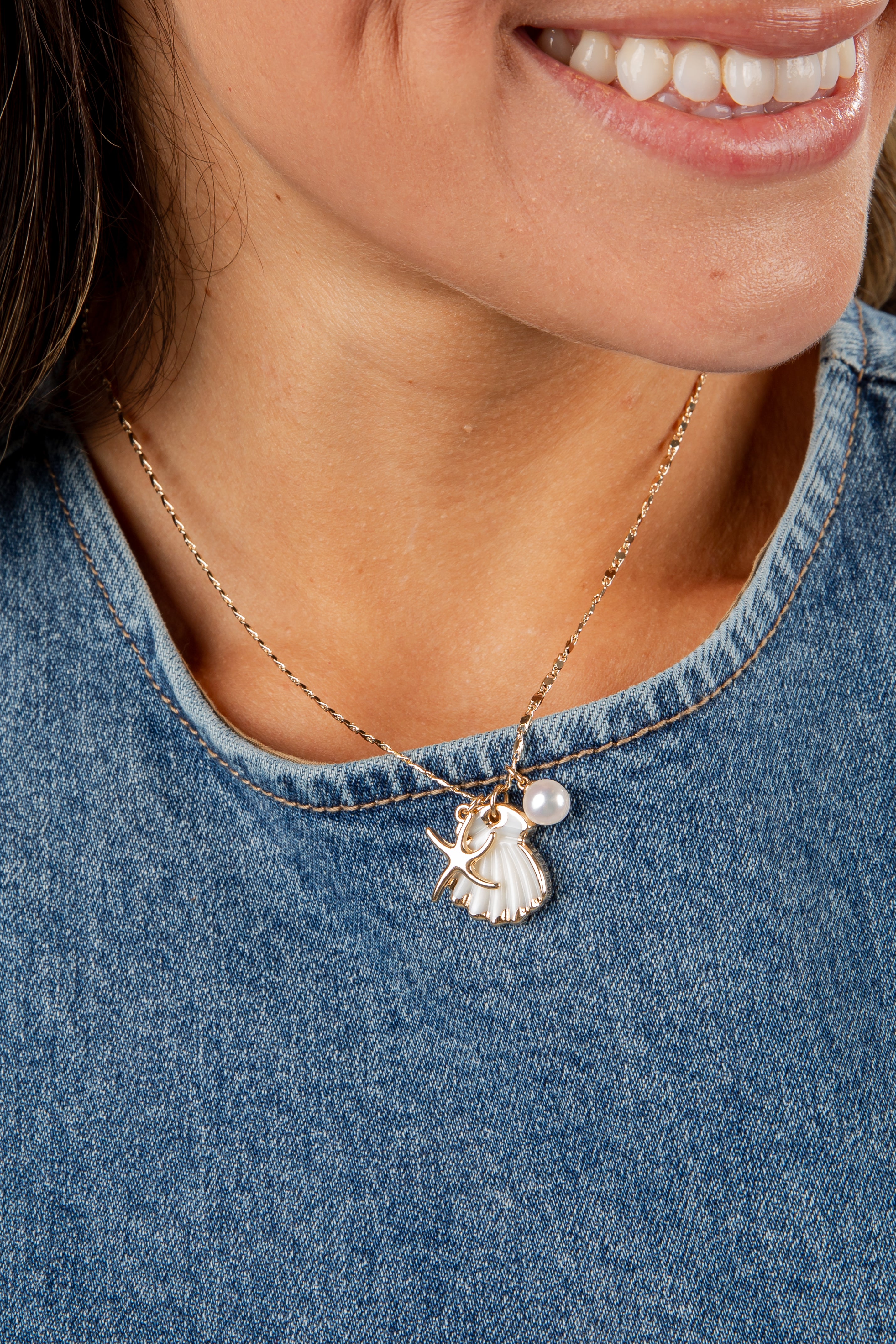 Close-up of a person wearing a necklace with a pendant, set against a denim background.