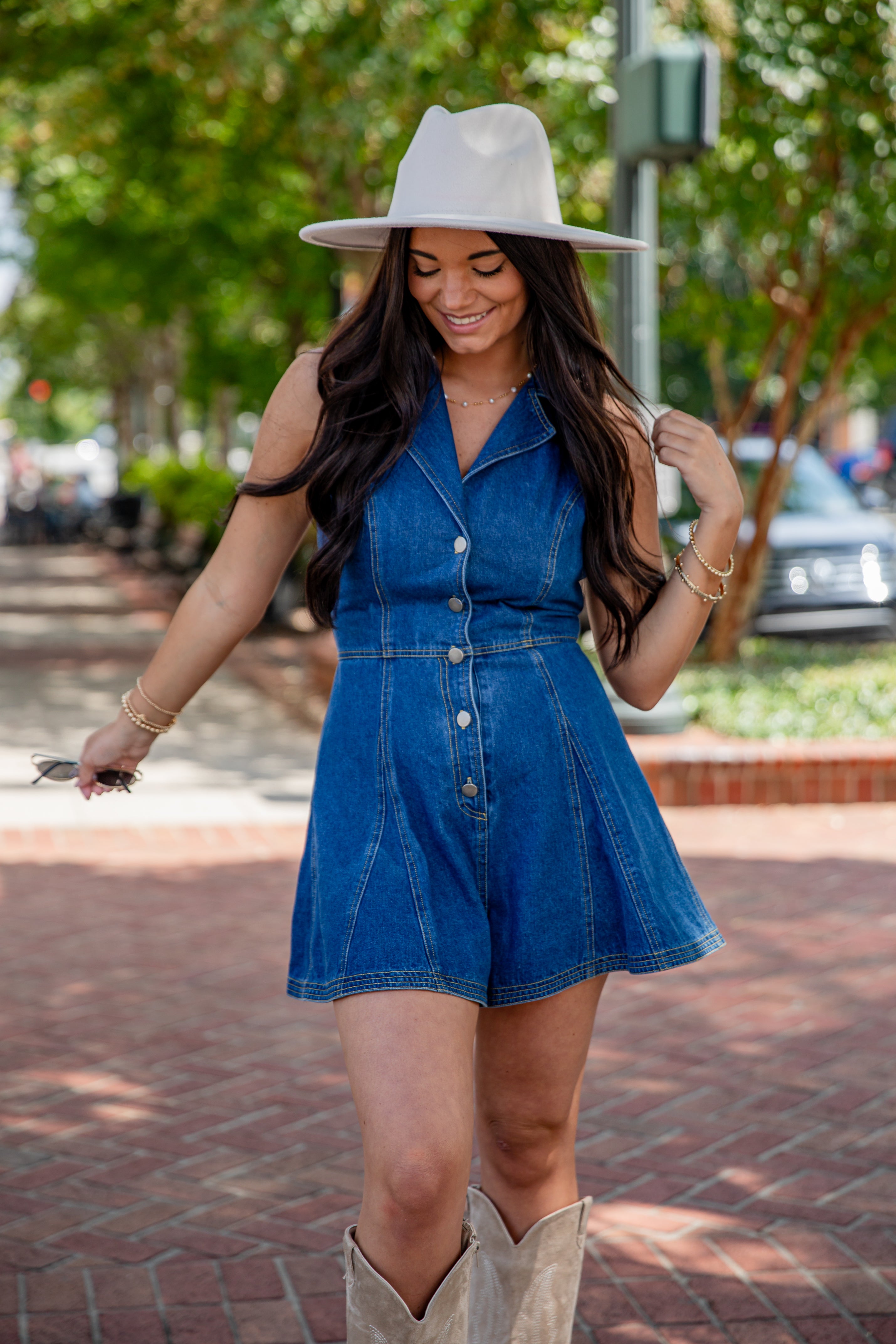 Woman wearing a blue denim dress and beige cowboy boots on a sidewalk.
