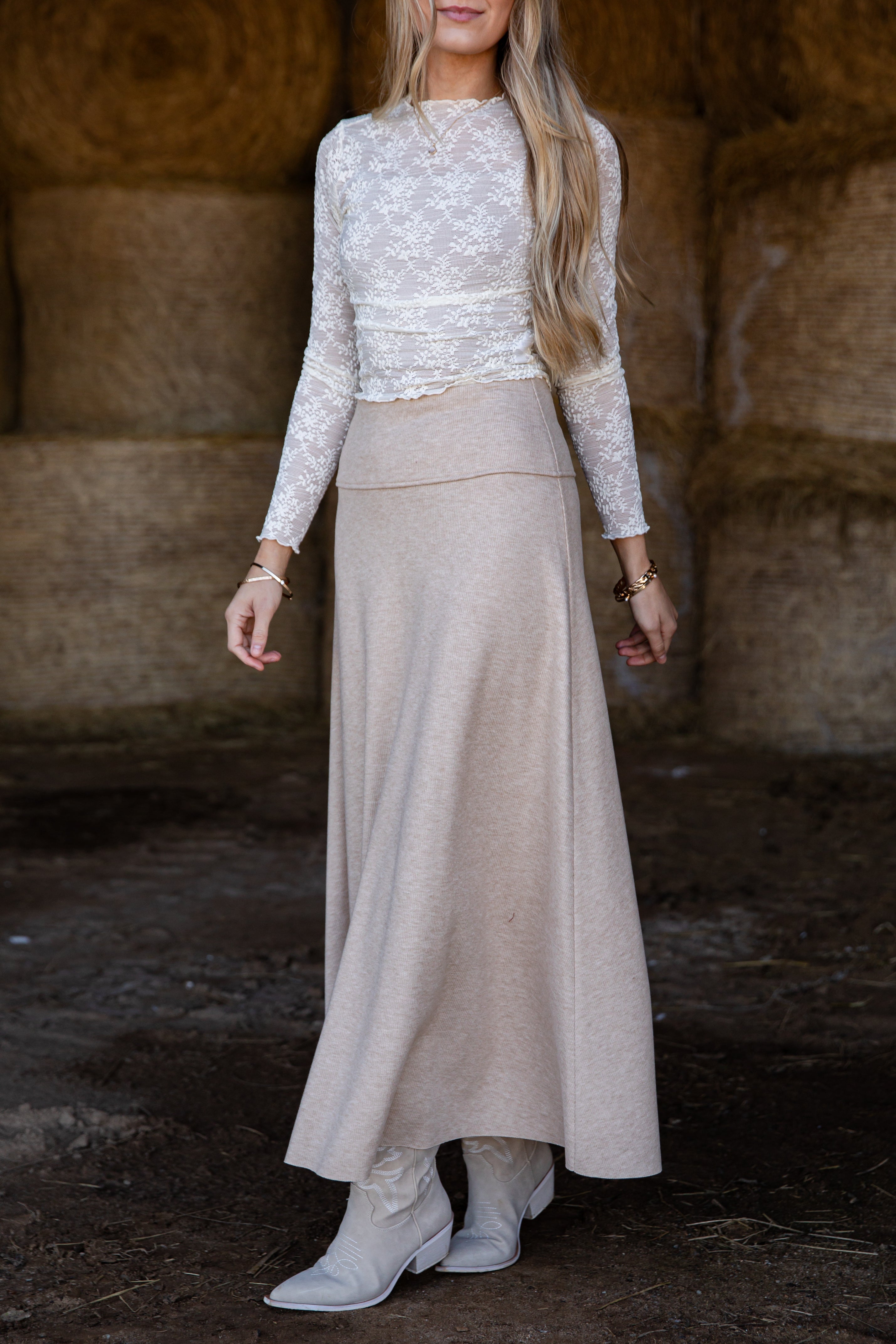Woman wearing a white lace top and beige skirt in a rustic setting