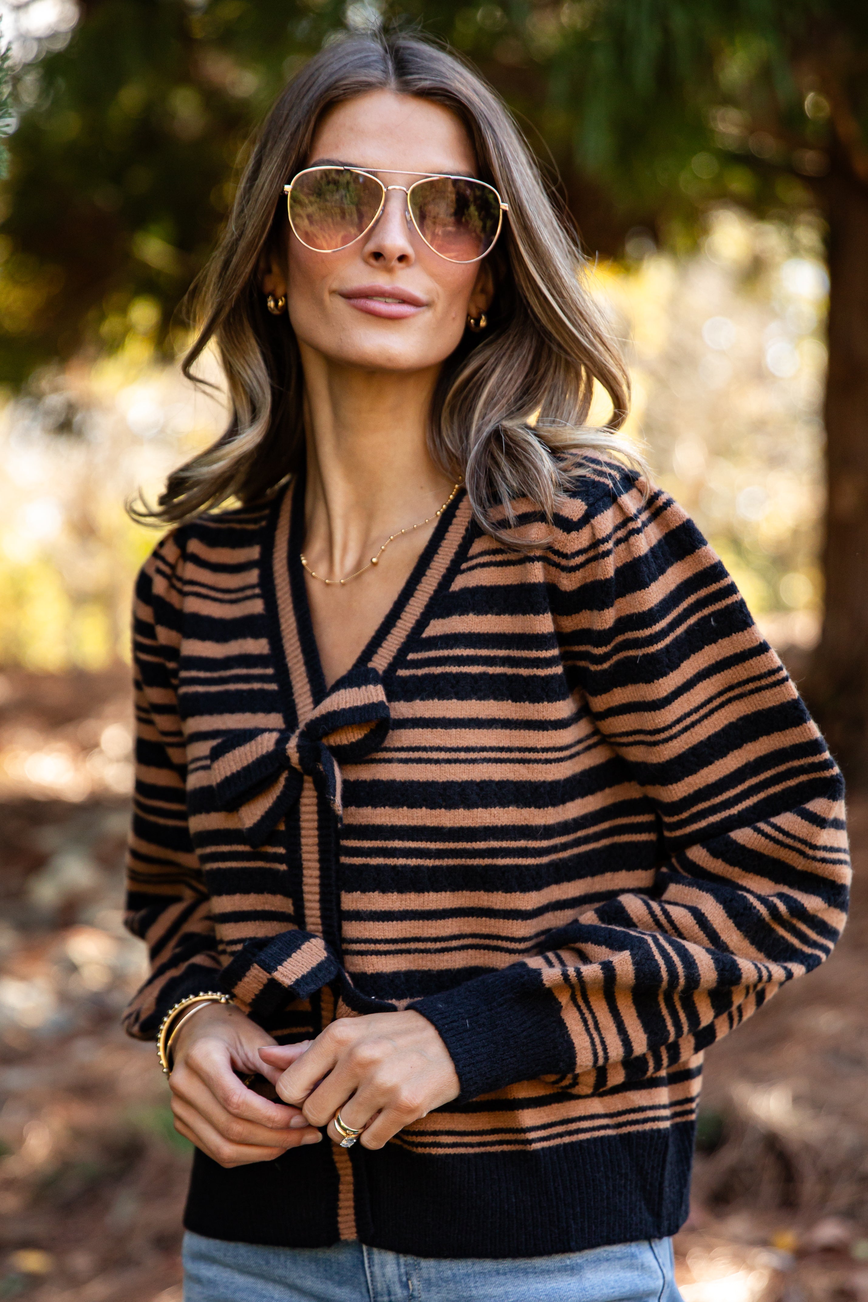 Woman wearing a striped sweater with sunglasses in a forest setting