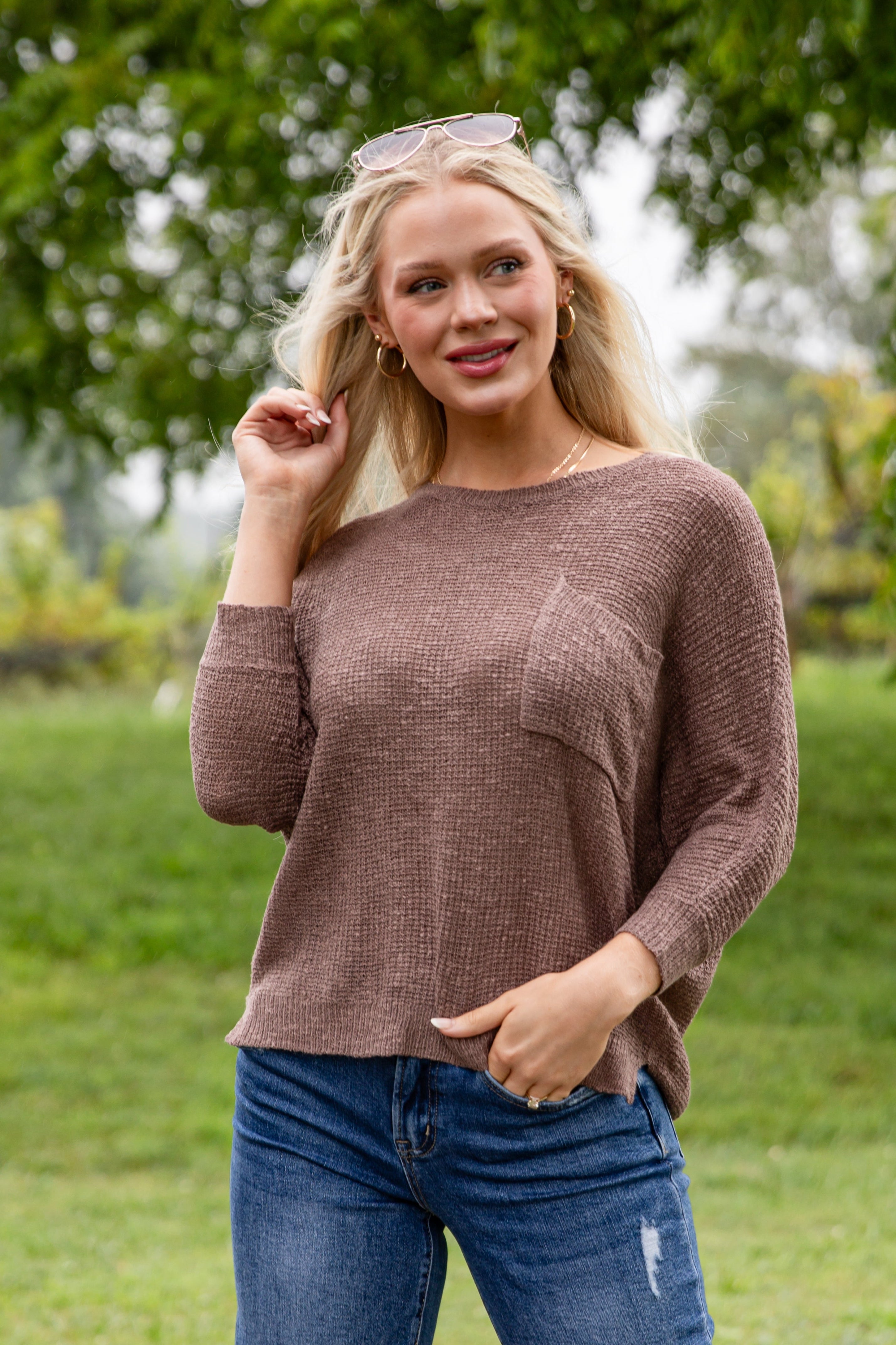 Woman wearing a brown sweater and blue jeans outdoors