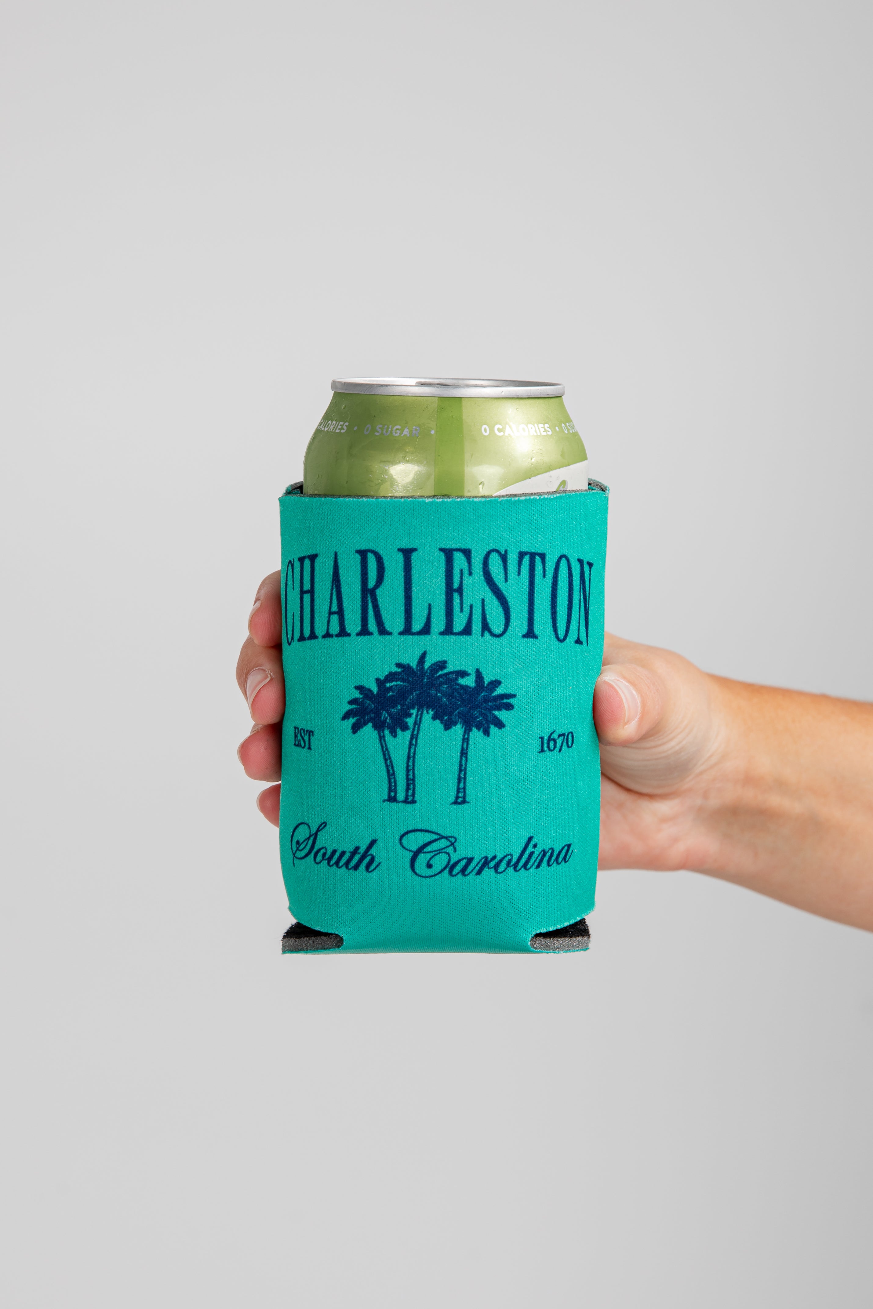 Hand holding a can with a teal Charleston, South Carolina design on a gray background