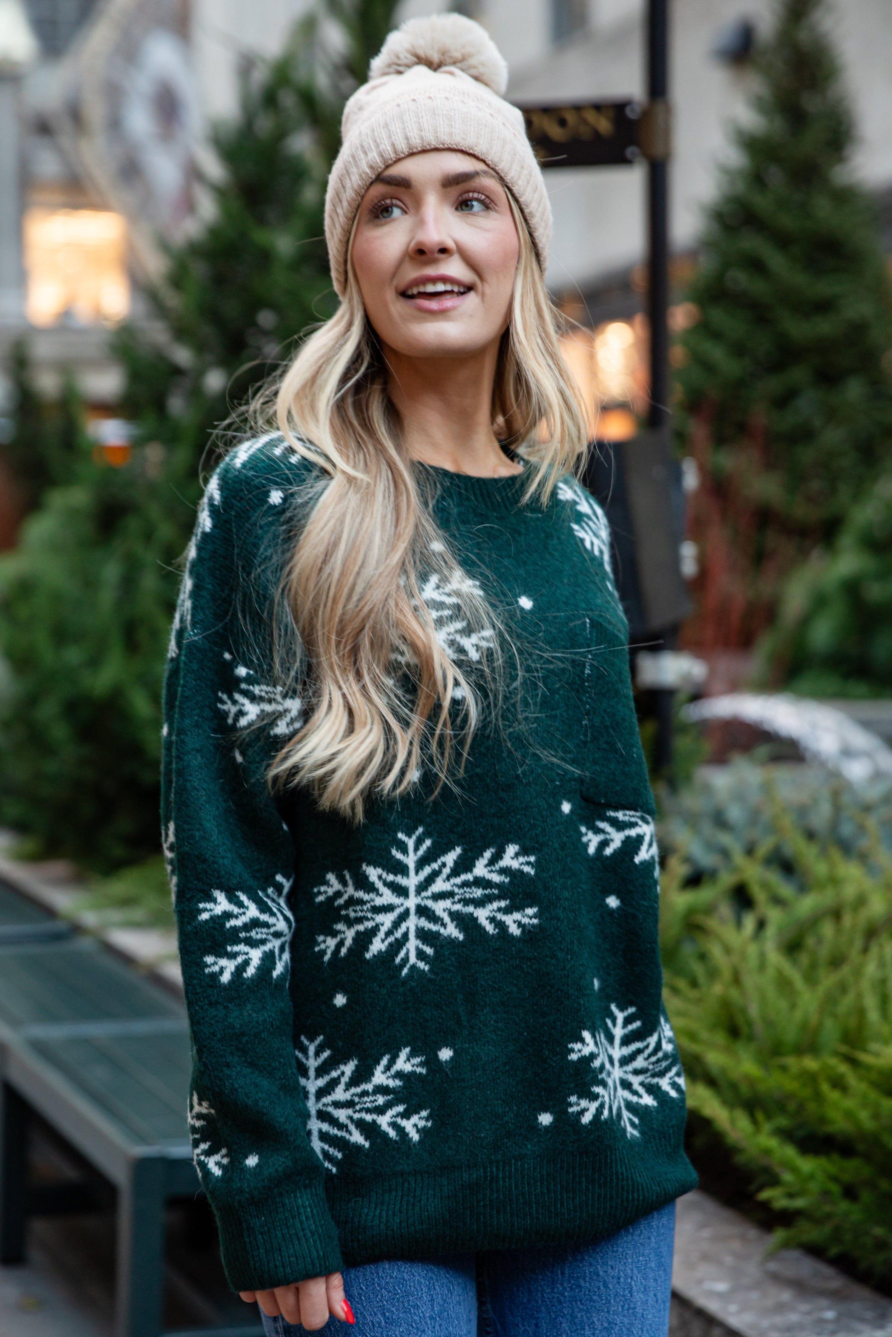 Woman wearing a green sweater with snowflake patterns and a beige beanie outdoors.