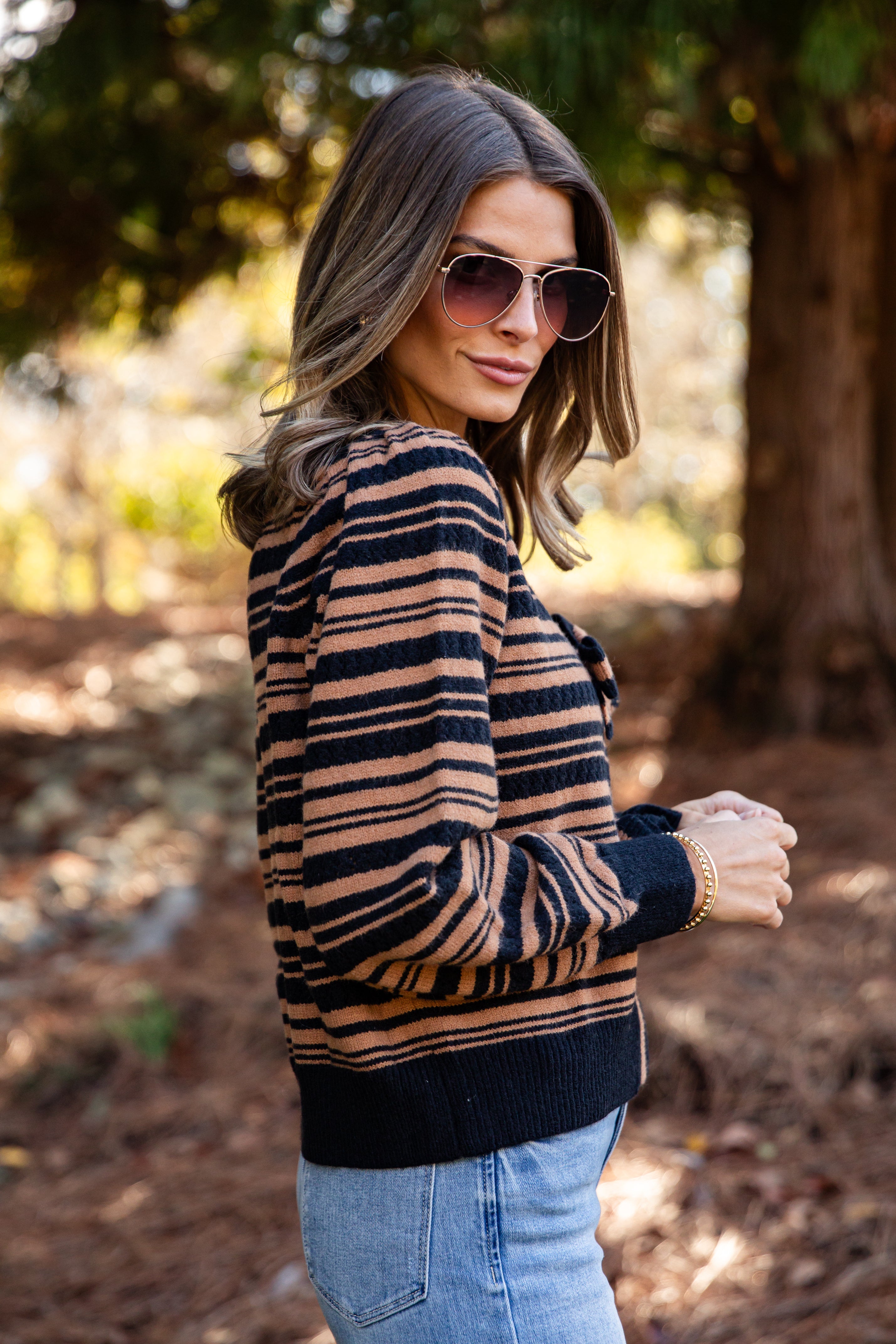 Woman wearing a striped sweater and sunglasses in a forest setting