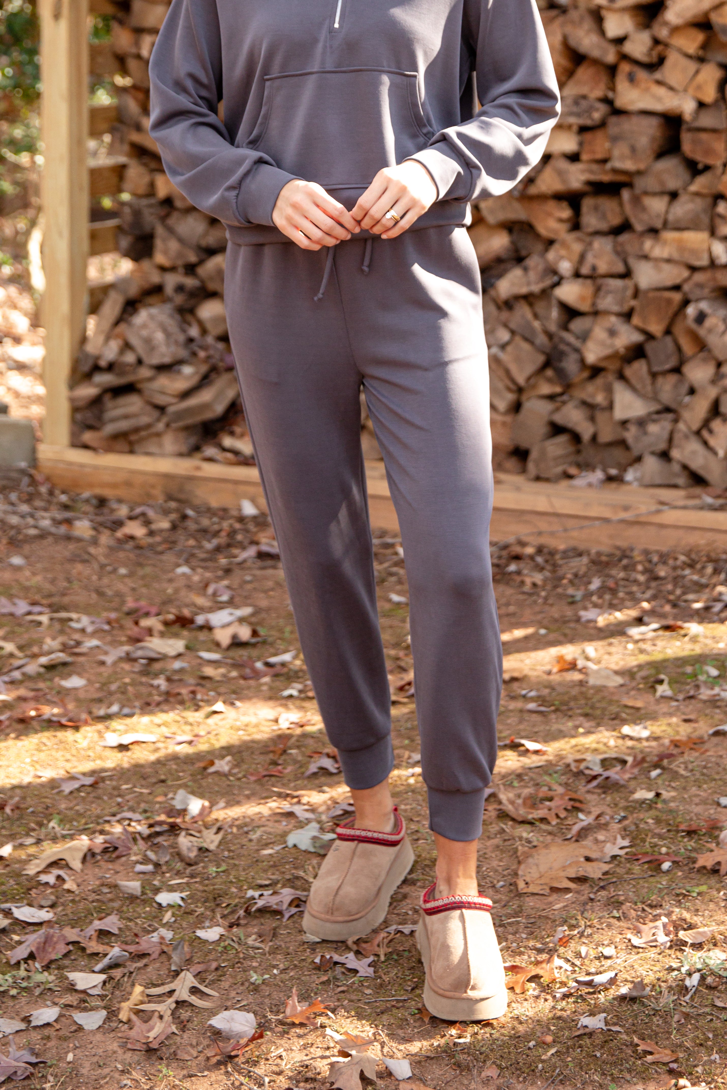Person wearing a gray tracksuit standing in front of stacked wood.