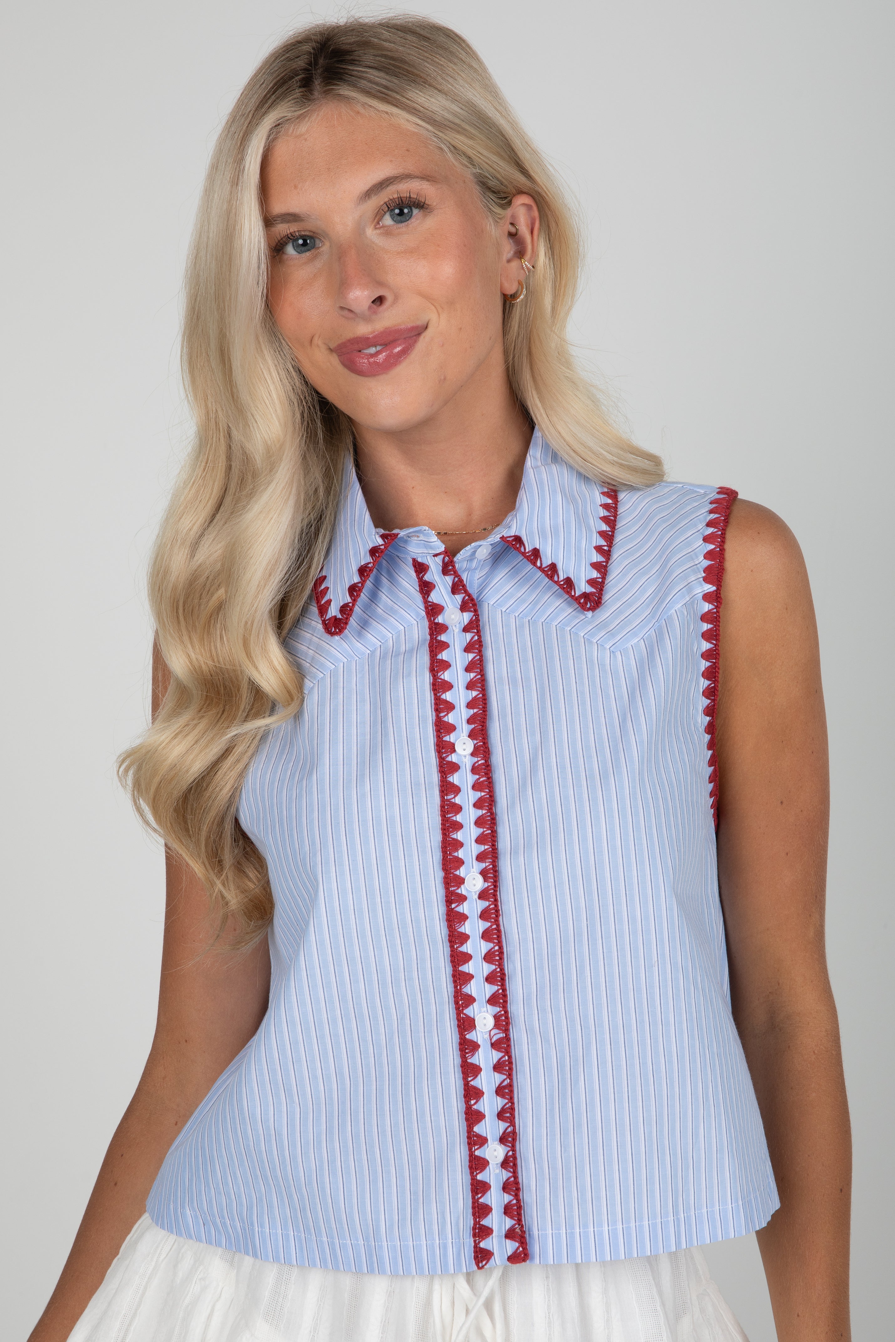 Woman wearing a light blue sleeveless blouse with red trim against a plain background
