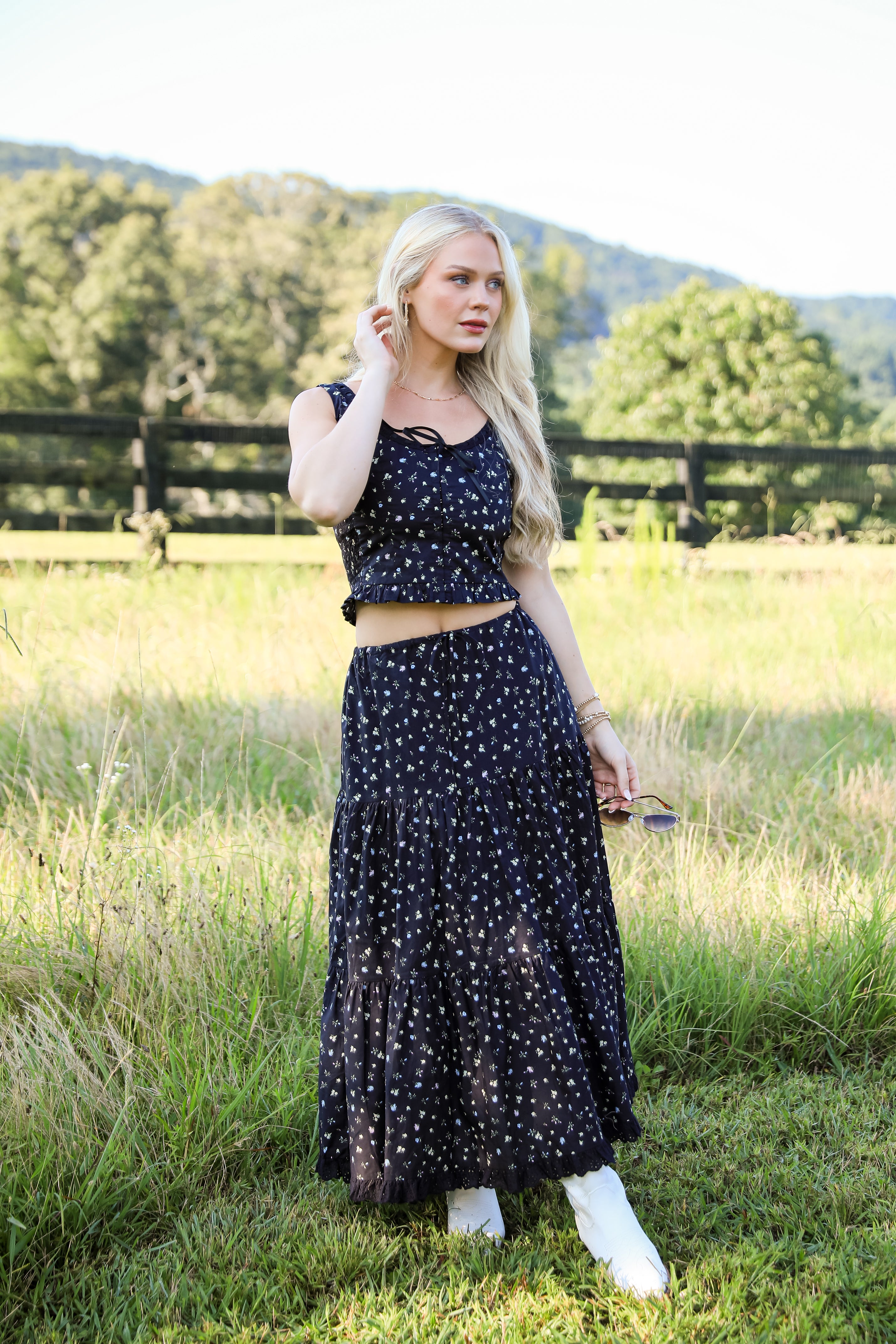 Woman in a black floral dress standing in a grassy field with trees in the background