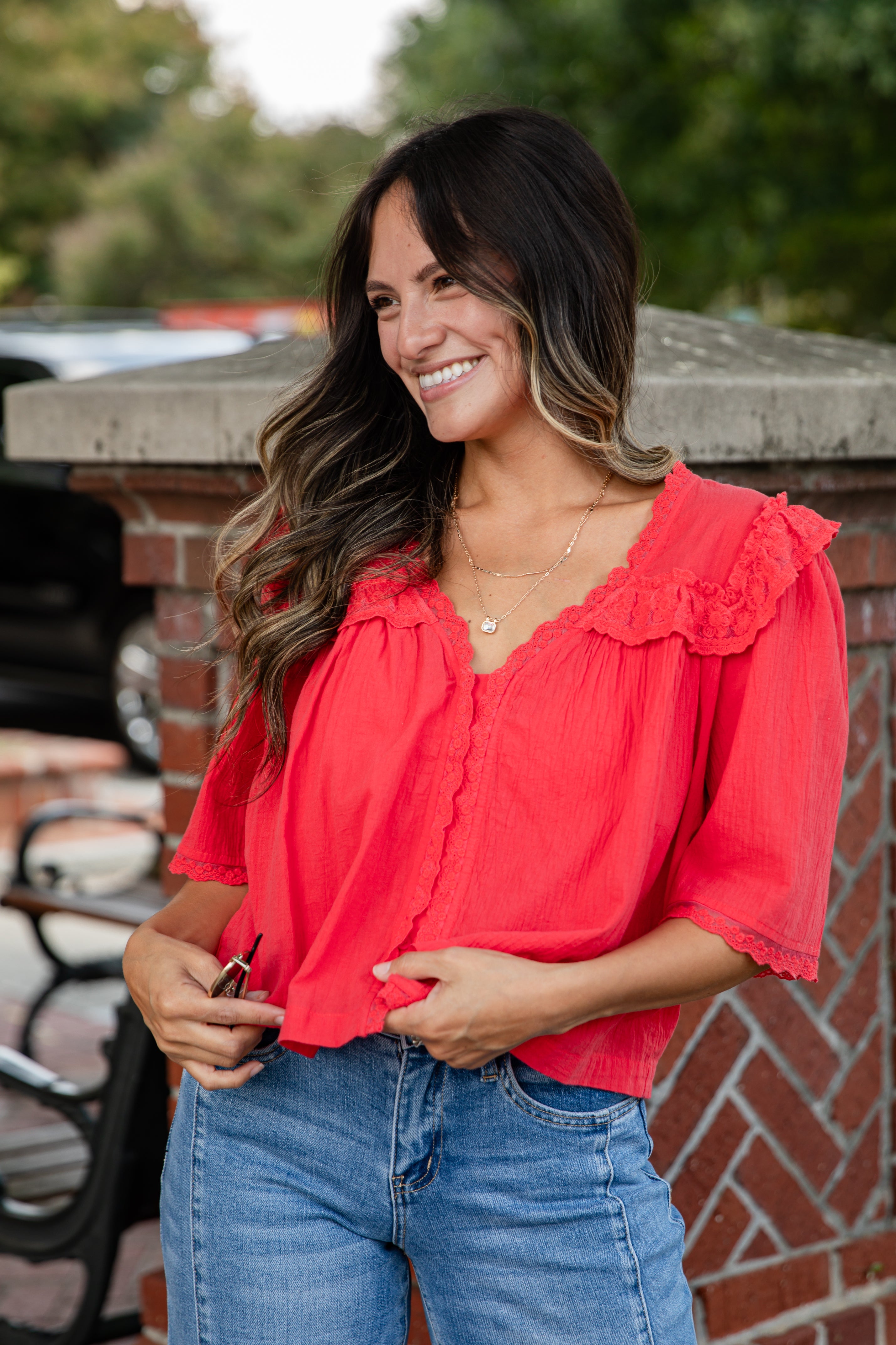 Woman wearing a red blouse and blue jeans standing outdoors.