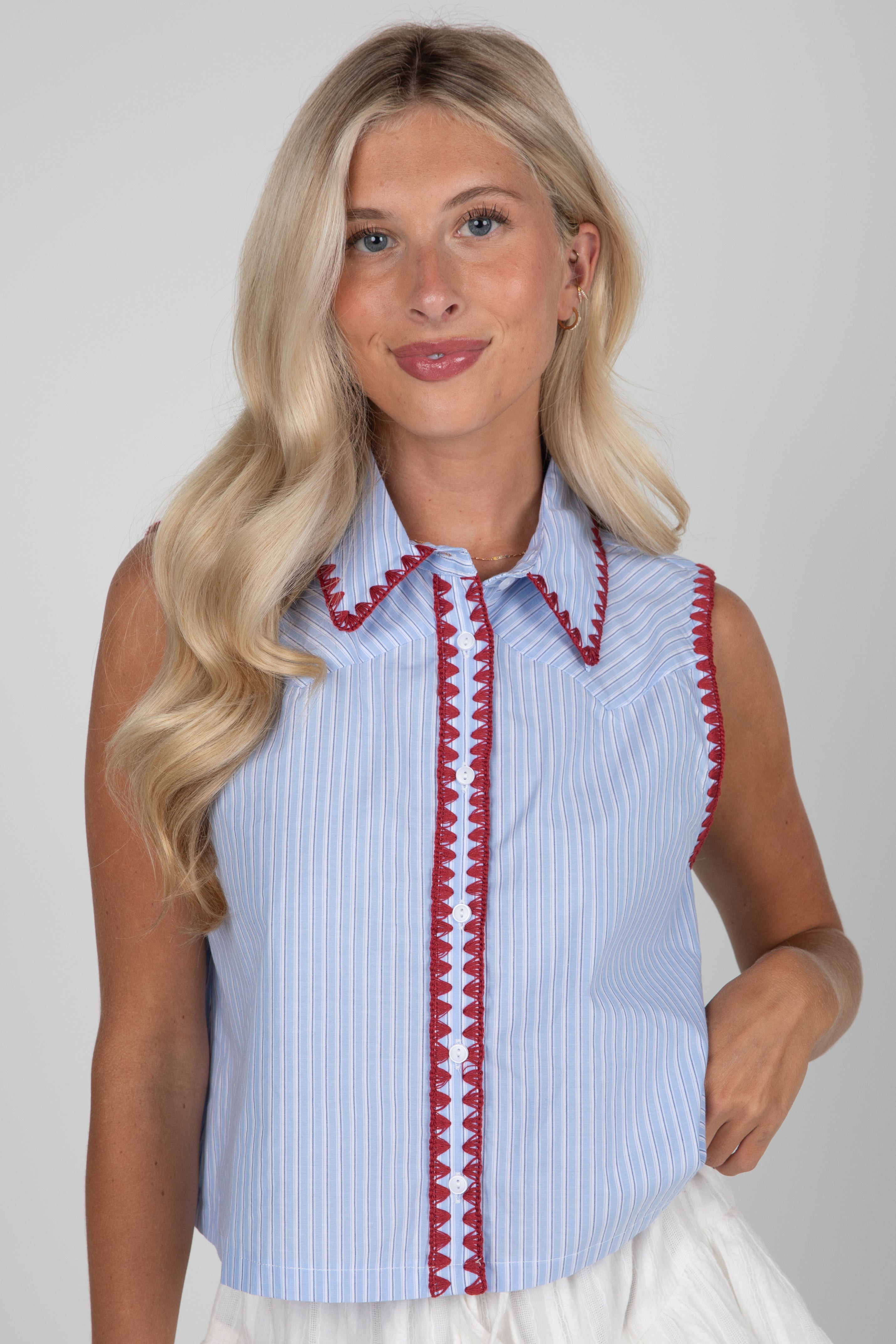 Woman wearing a sleeveless blue and white striped shirt with red trim on a plain background