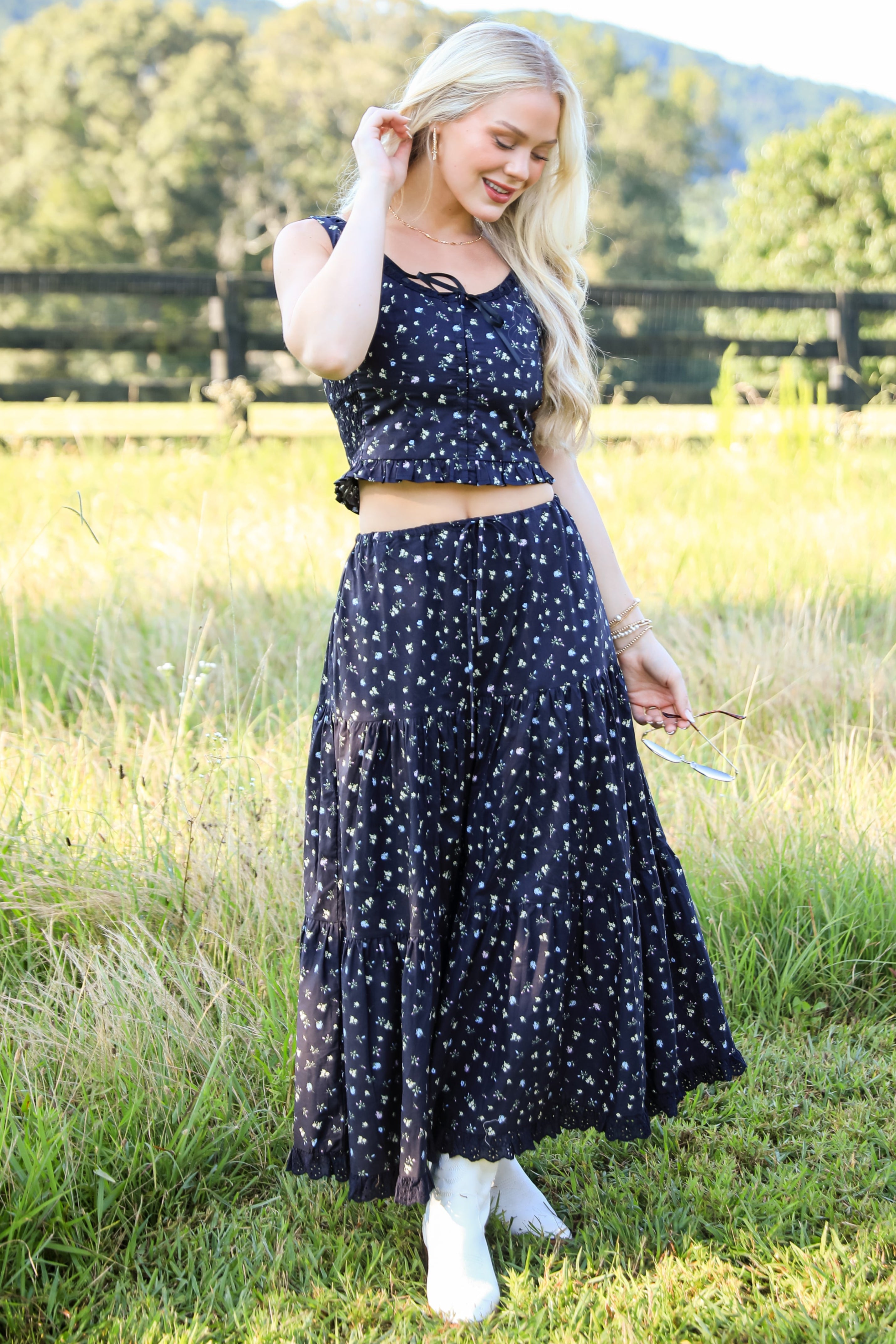 Woman wearing a navy blue floral dress standing in a grassy field with mountains in the background