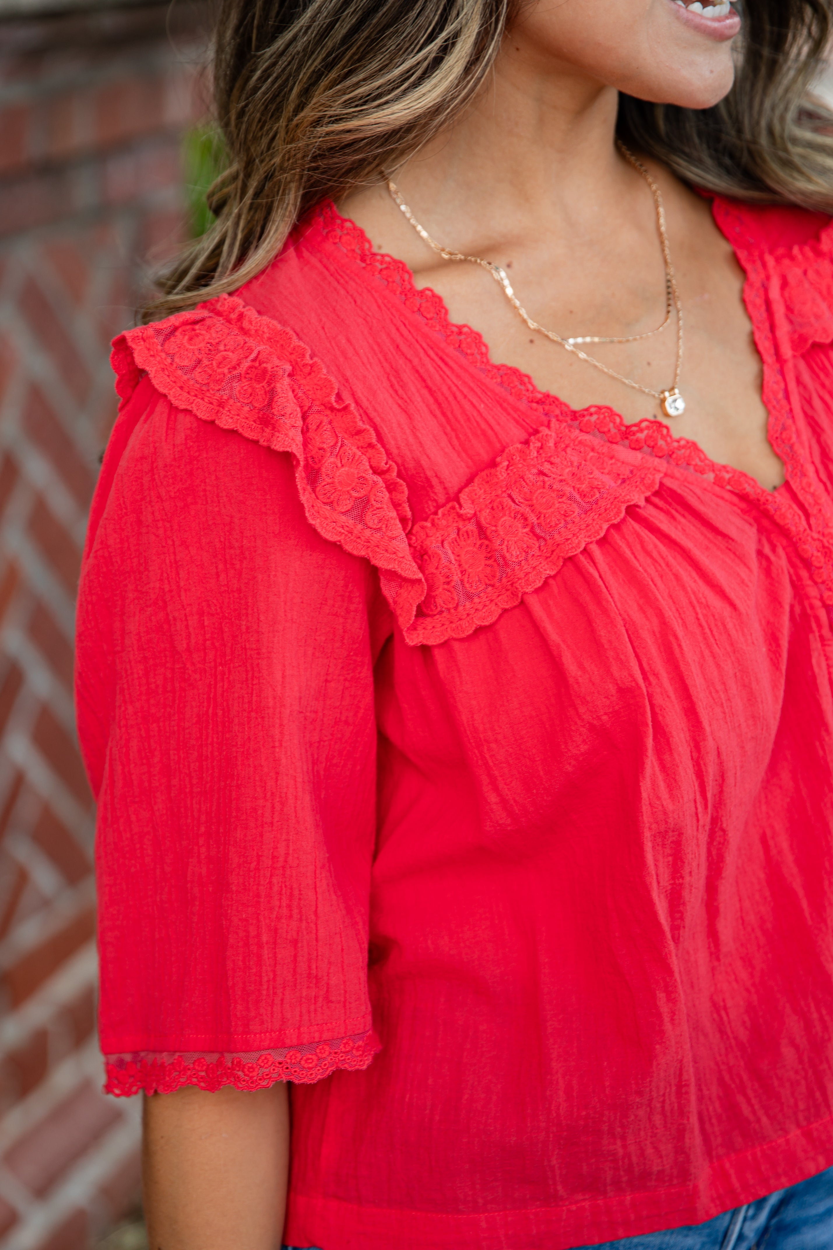 Red blouse with lace details worn by a person, against a blurred background