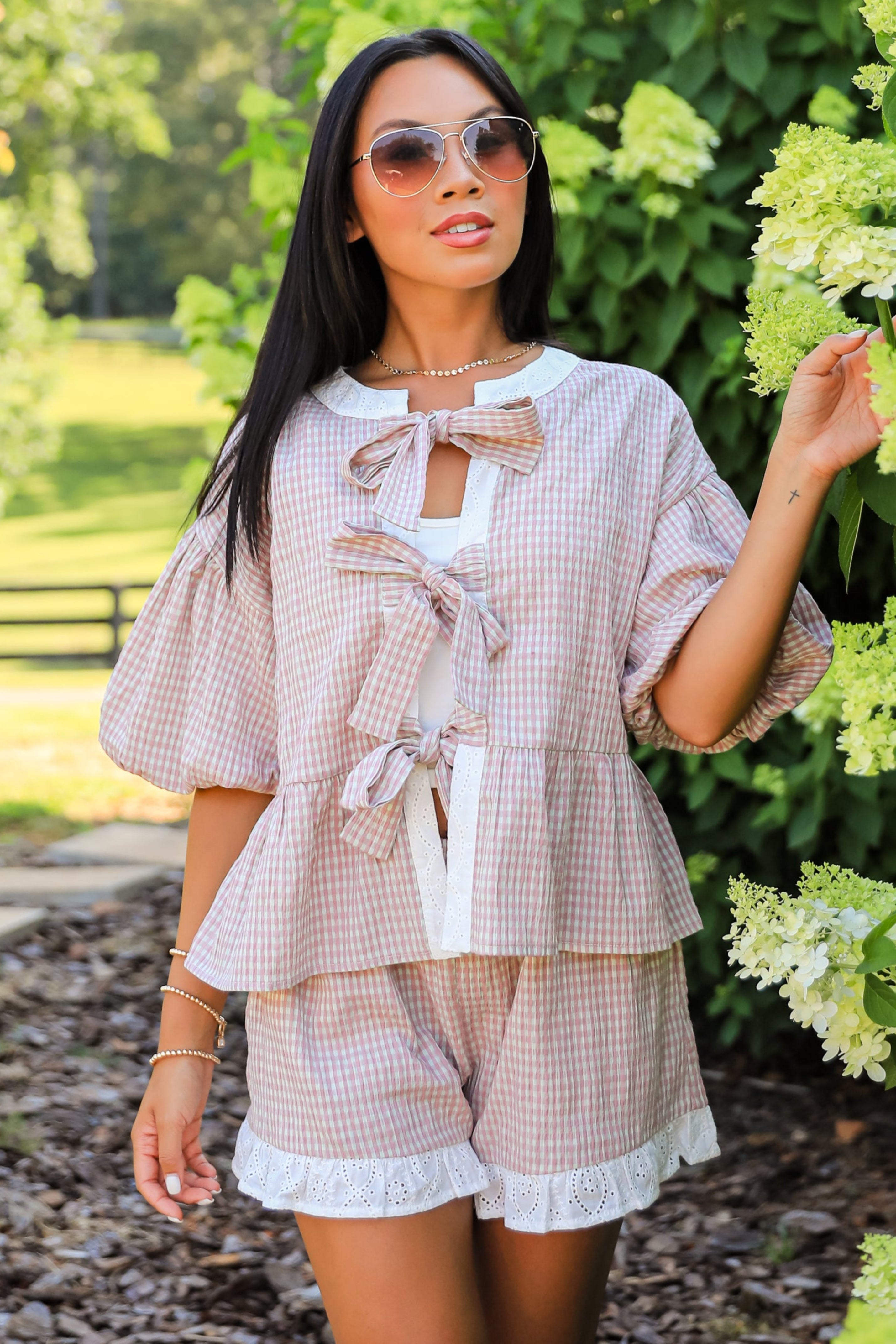 Woman in a light outfit standing in a garden with greenery and flowers.