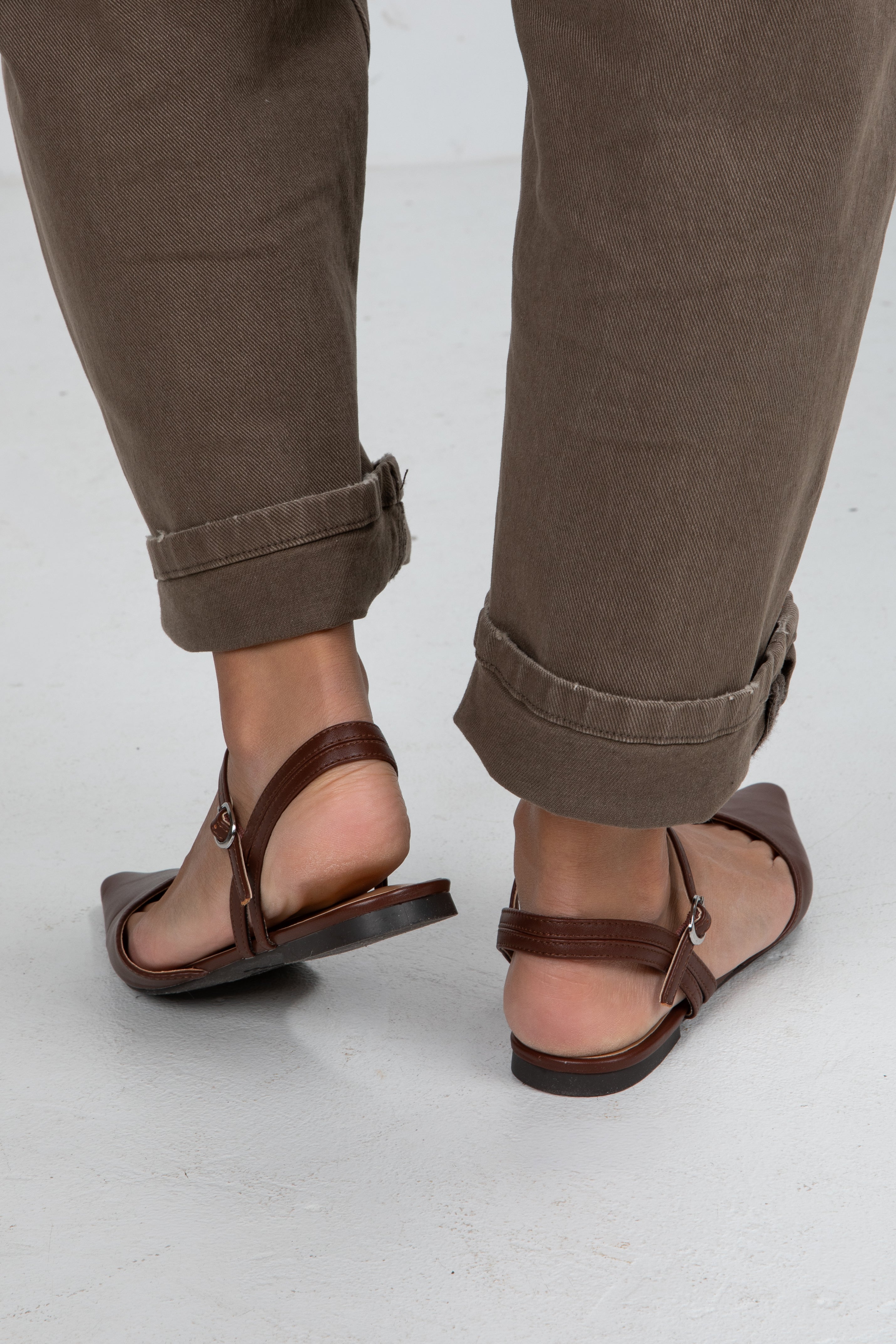 Brown sandals worn with rolled-up brown pants on a light gray background