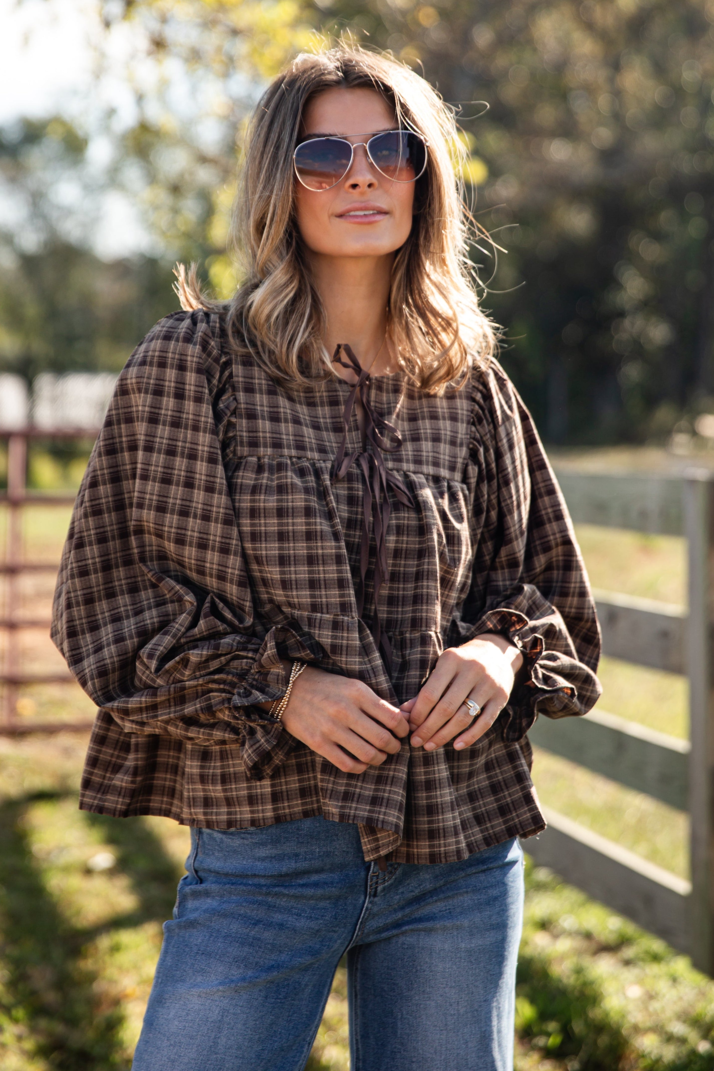 Woman wearing a plaid shirt and sunglasses outdoors with trees in the background