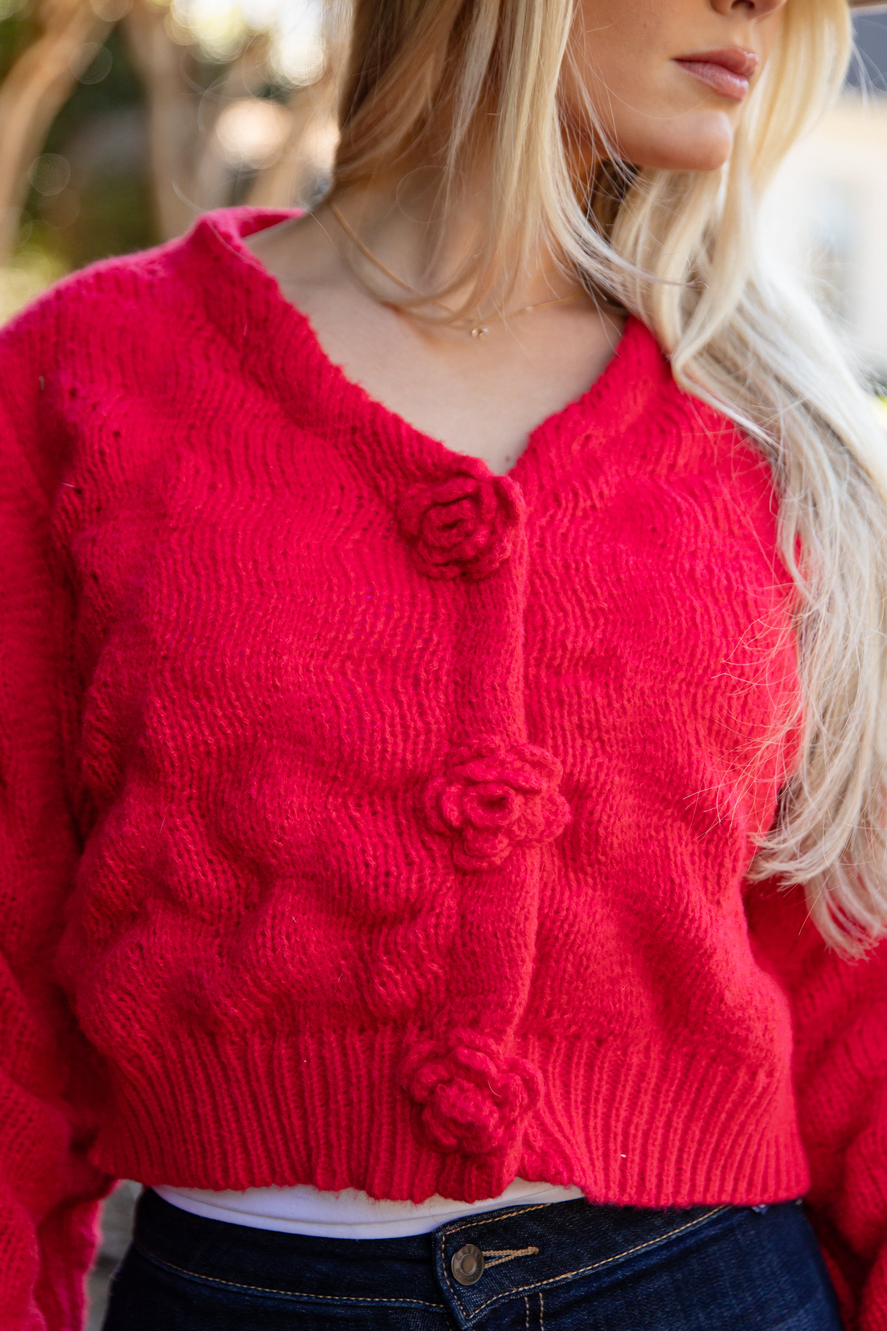 Person wearing a red knitted cardigan with floral buttons.