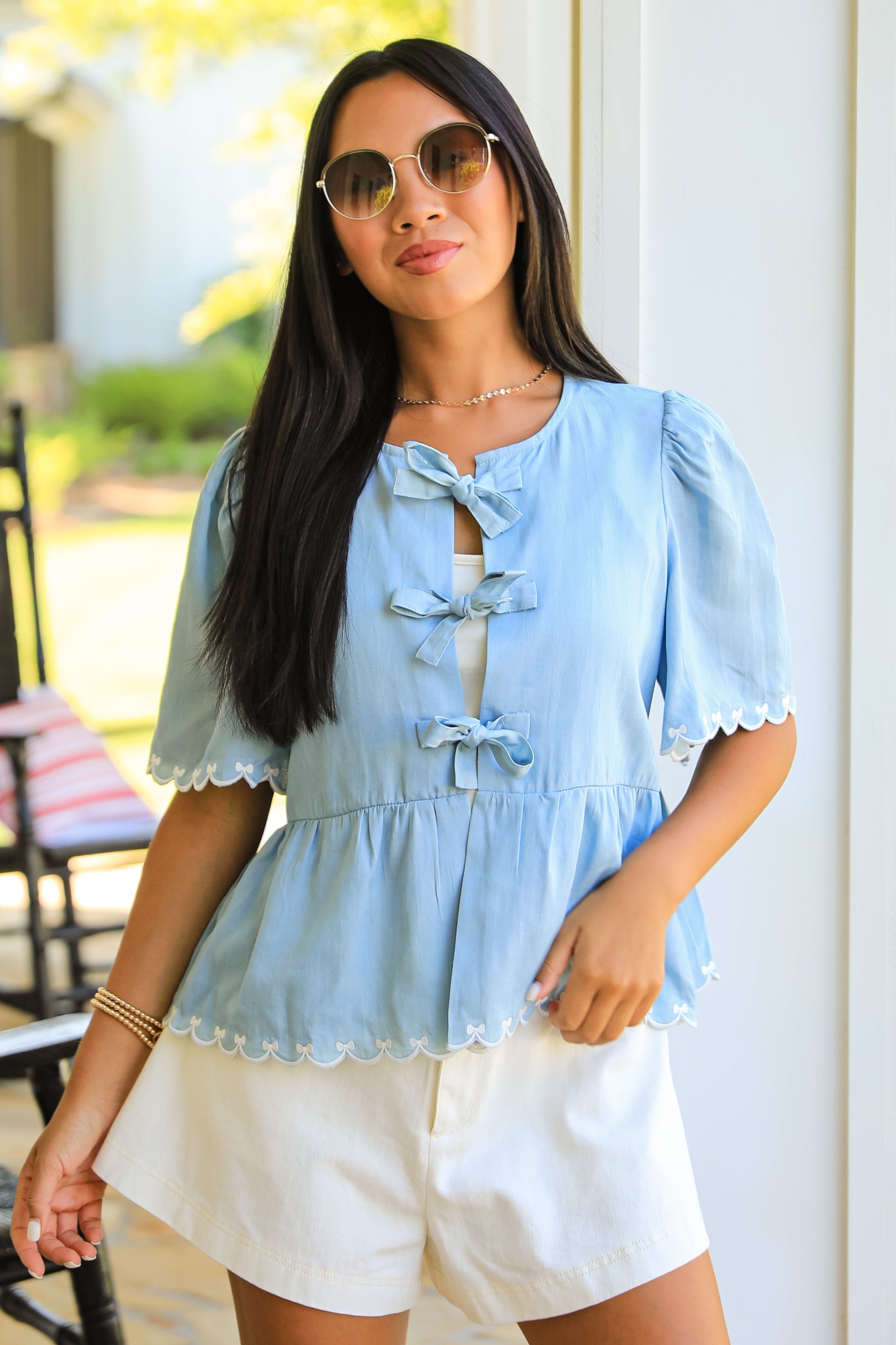 Woman wearing a light blue top and white shorts standing outdoors.