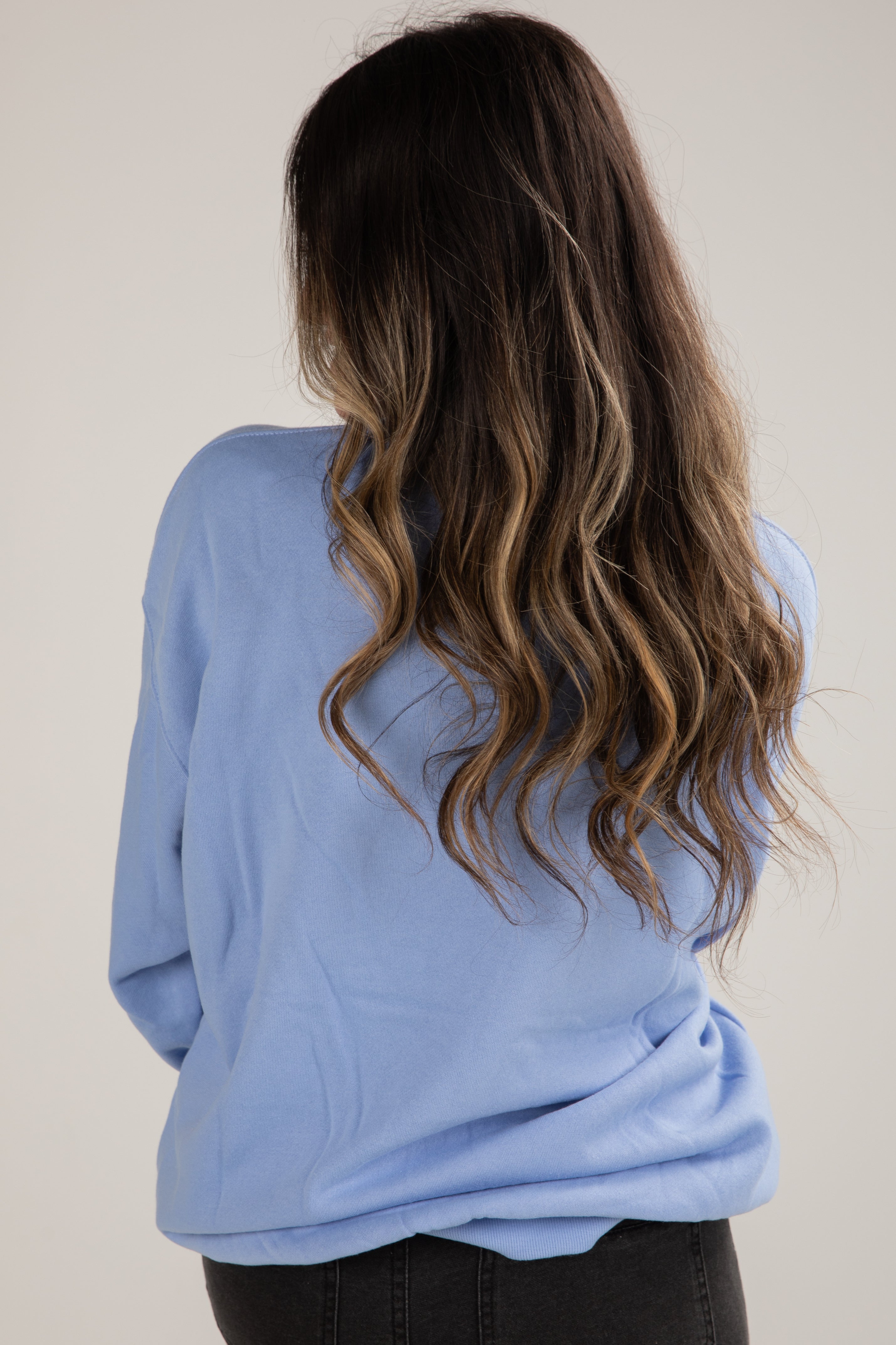 Person wearing a light blue sweater with long, wavy hair on a plain background