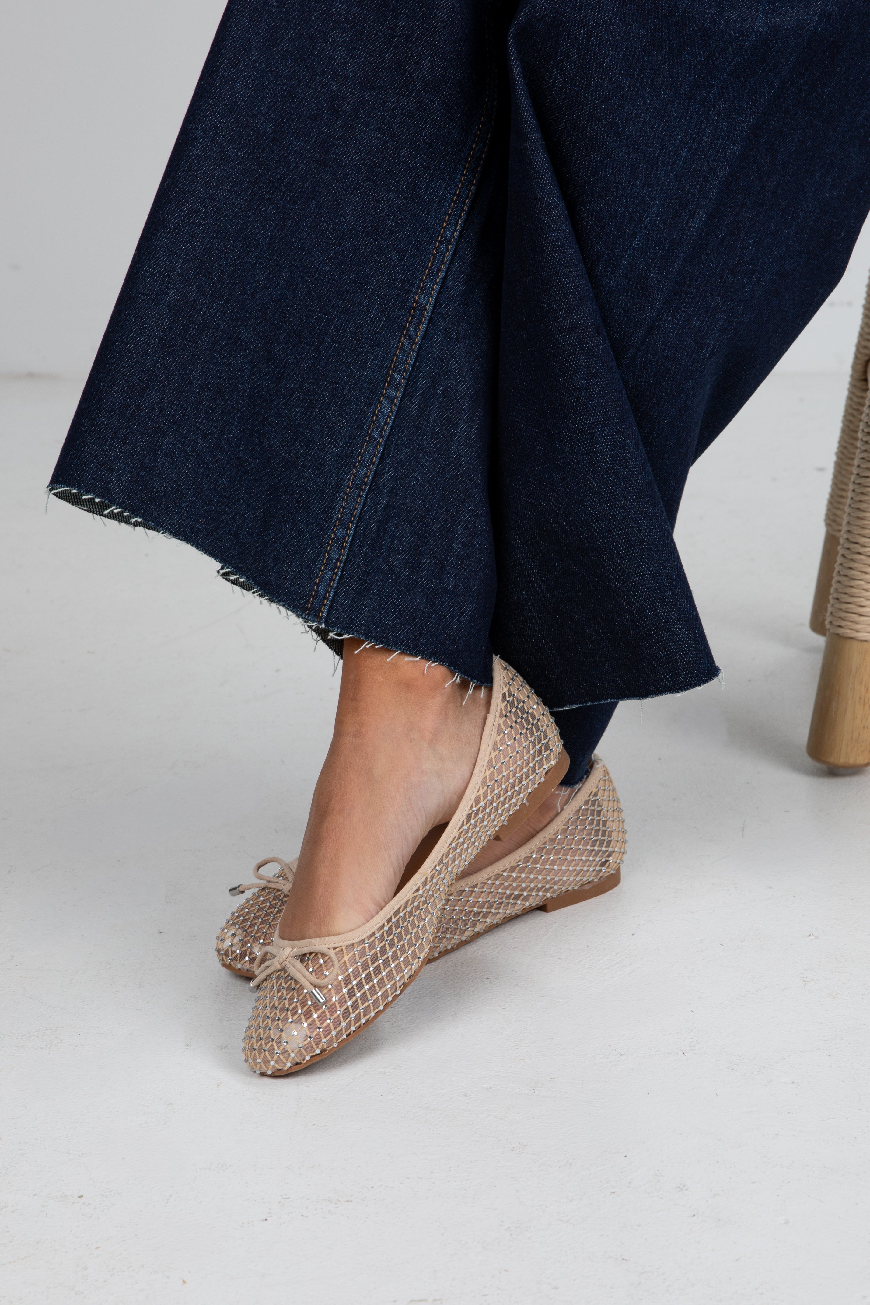 Beige mesh flats worn with dark blue jeans on a light gray background