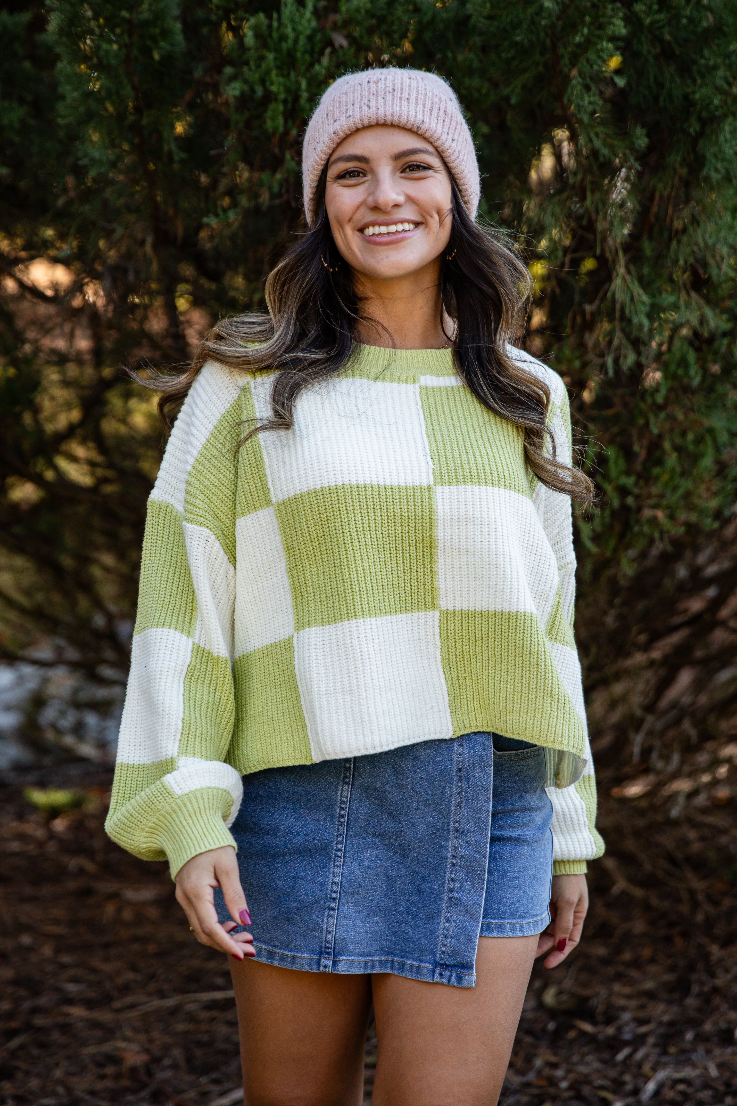 Woman wearing a checkered sweater and denim skirt standing in a forest setting