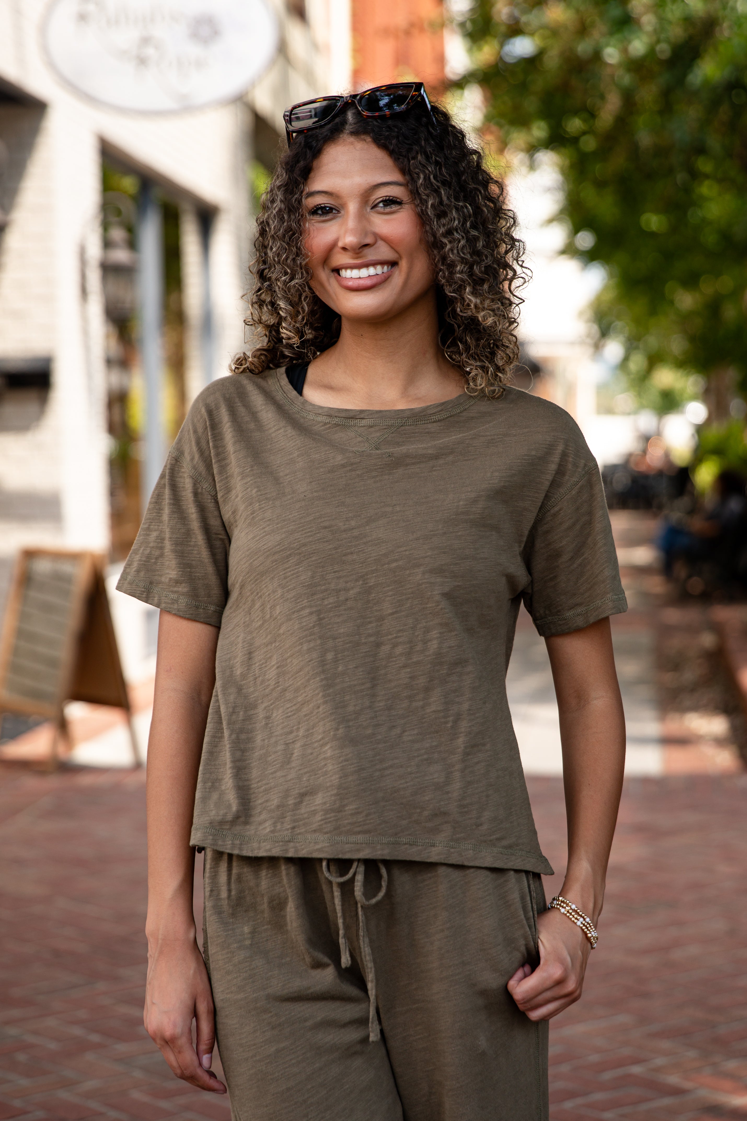 Woman wearing an olive green t-shirt and pants on a street.