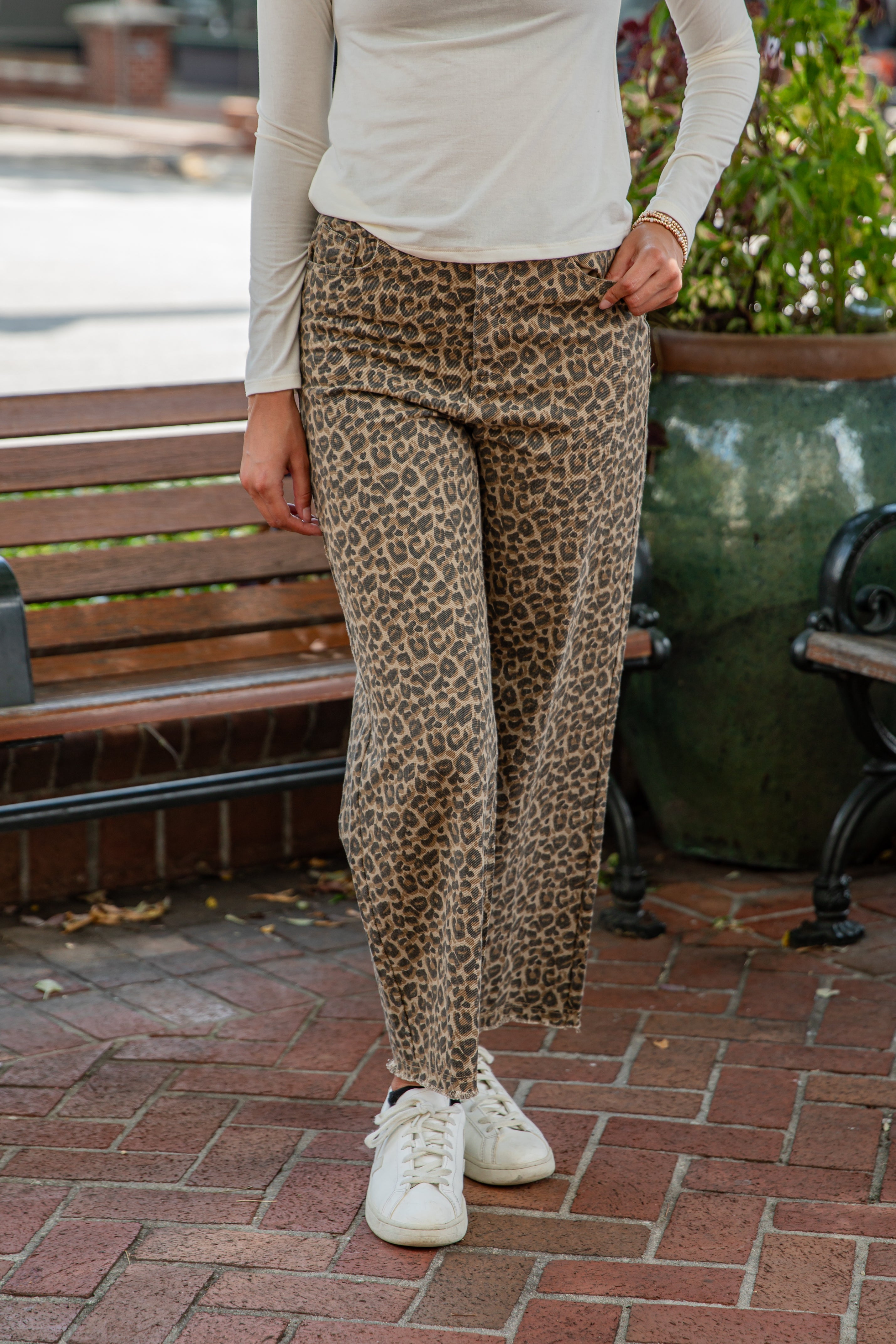 Person wearing leopard print pants and white sneakers on a brick pavement.
