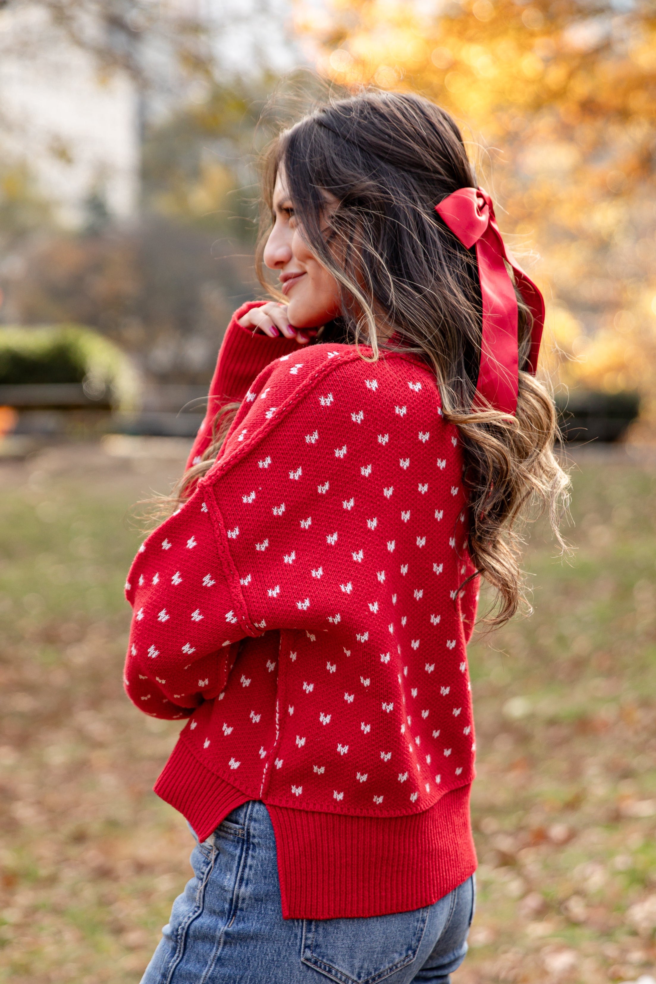 Woman wearing a red sweater with white patterns and blue jeans, standing in an autumn setting.