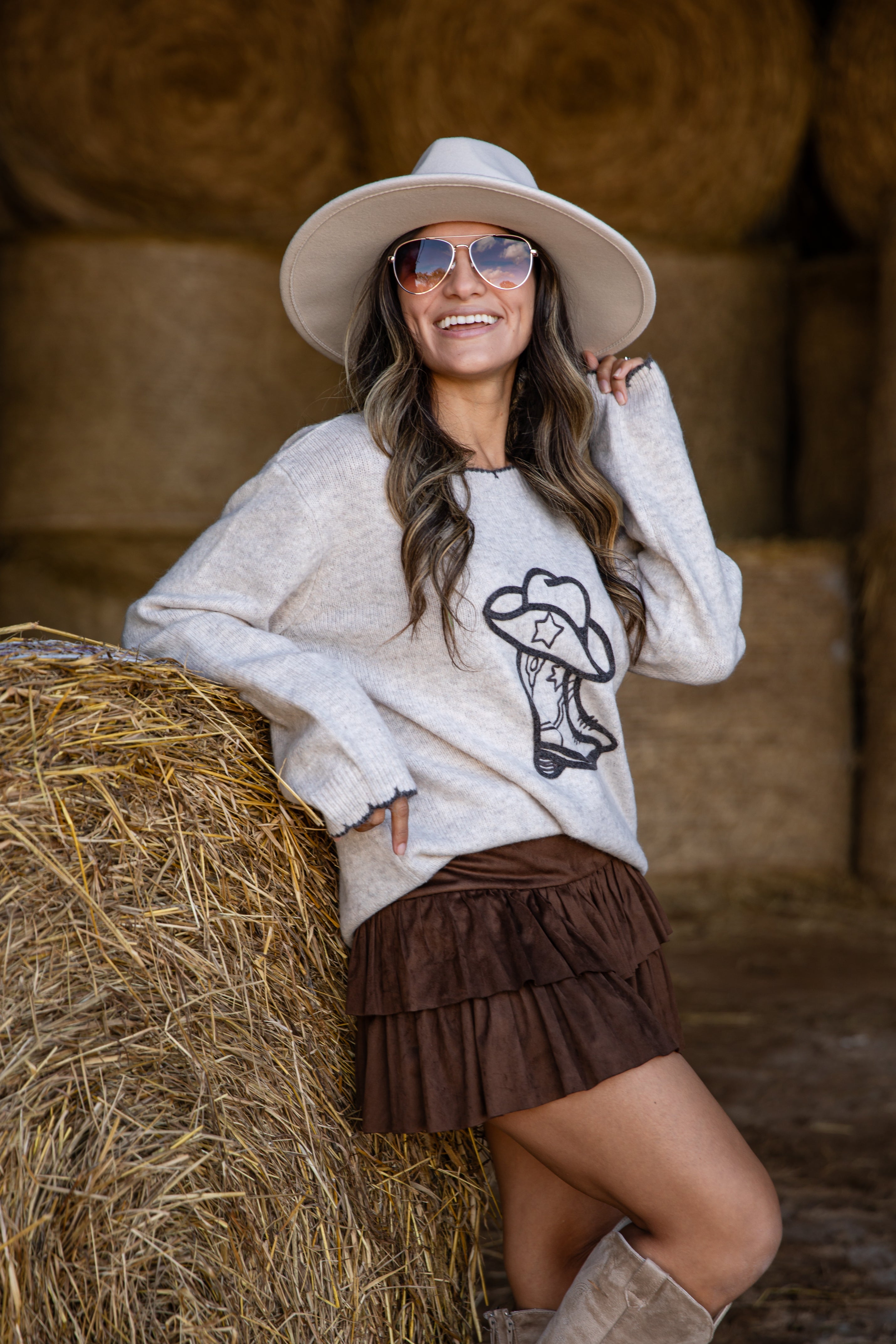 Woman in a sweater and hat standing next to a hay bale in a barn setting