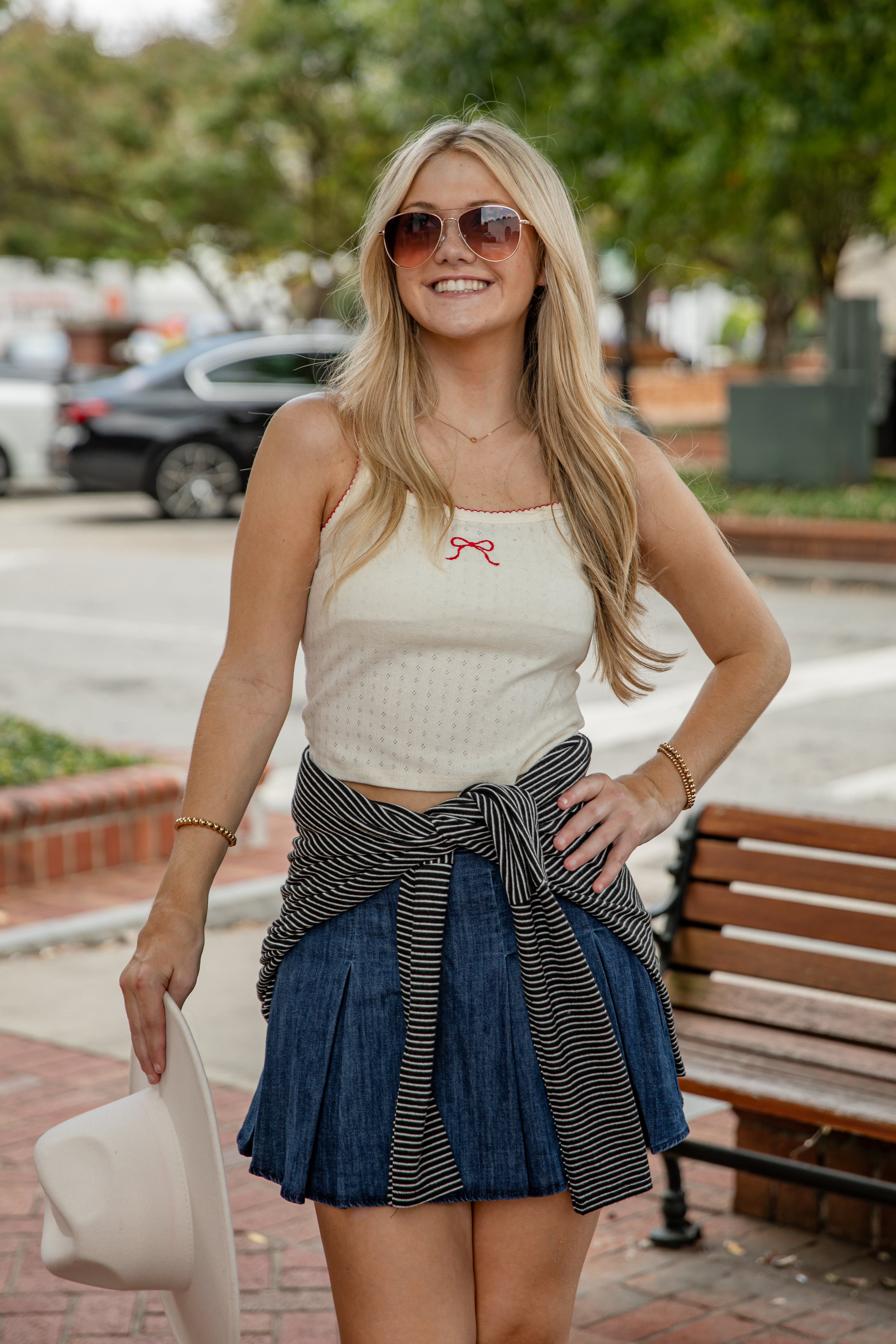 Woman wearing a cream tank top with a red bow and a blue skirt outdoors.