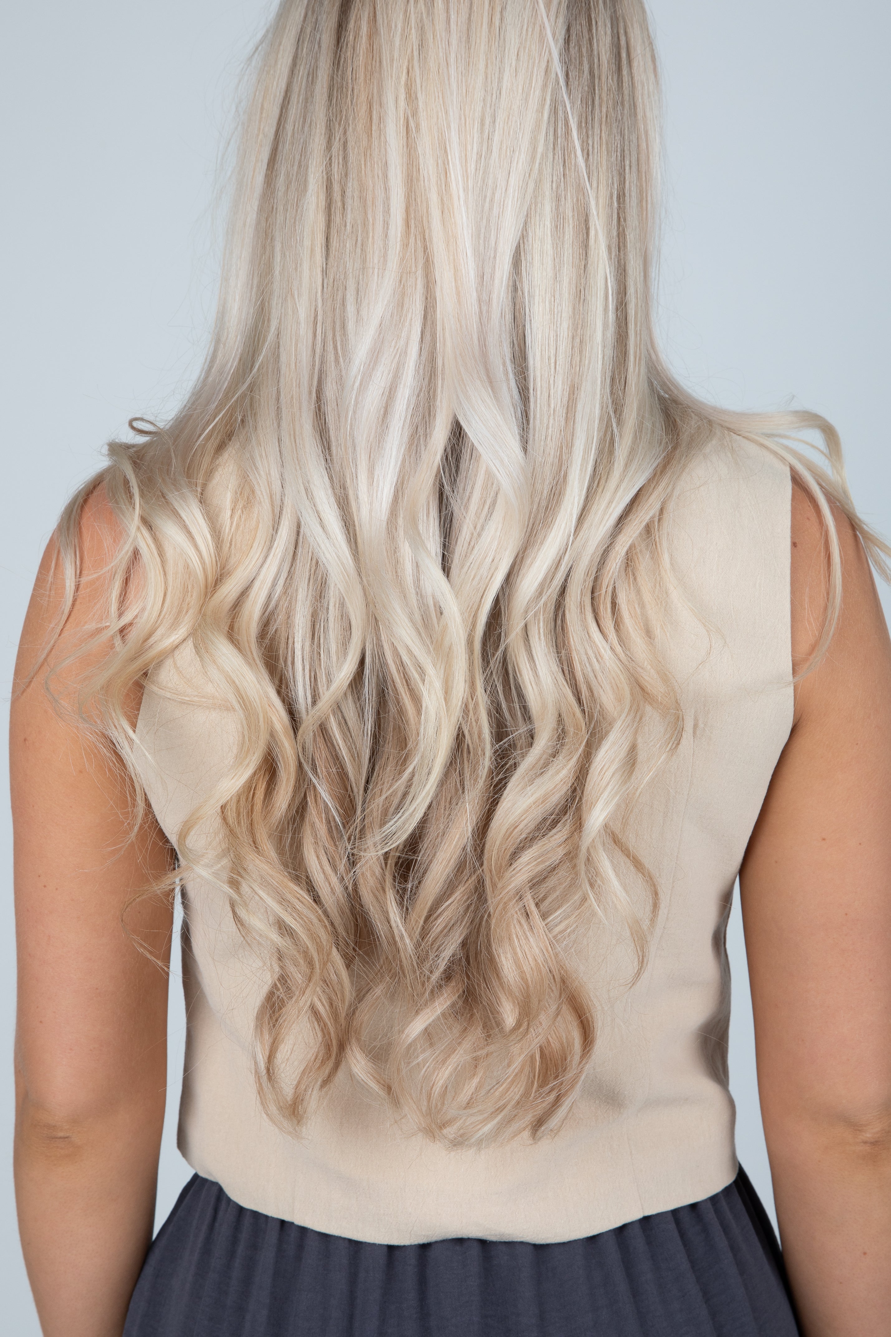 Person with long, wavy blonde hair wearing a beige sleeveless top against a plain background