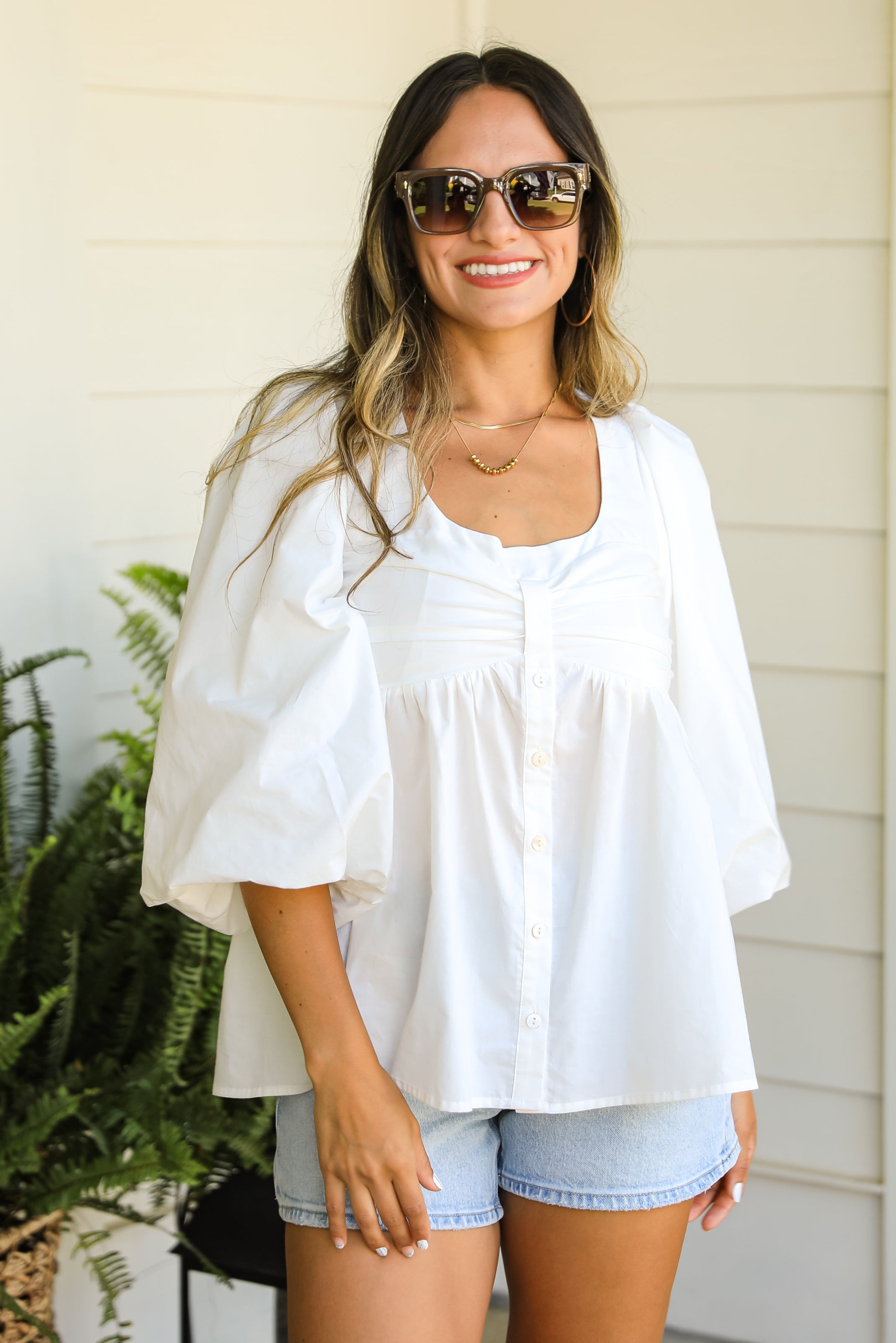 Woman wearing a white blouse and denim shorts standing outdoors.