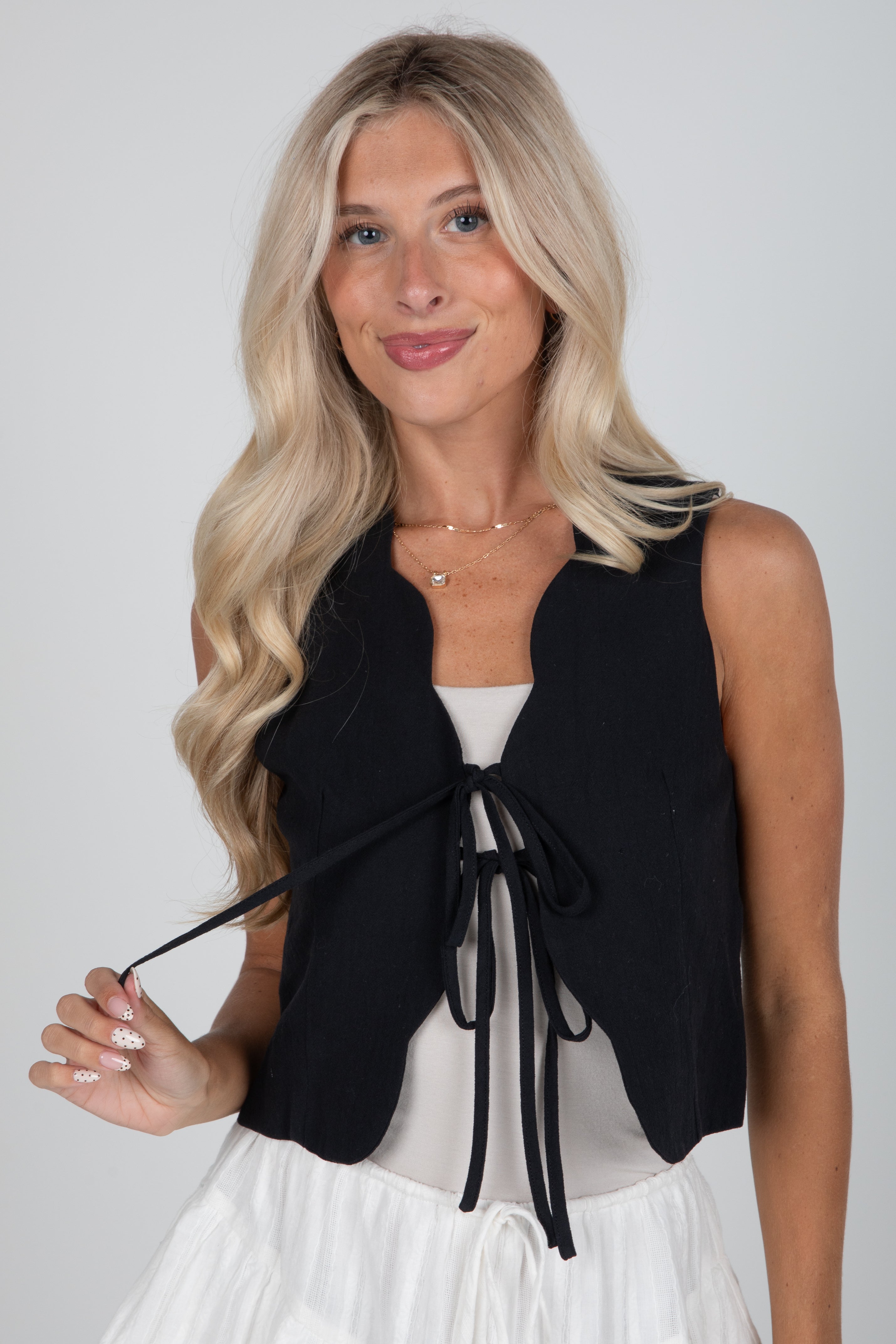 Woman wearing a black sleeveless top with a tie detail on a white background