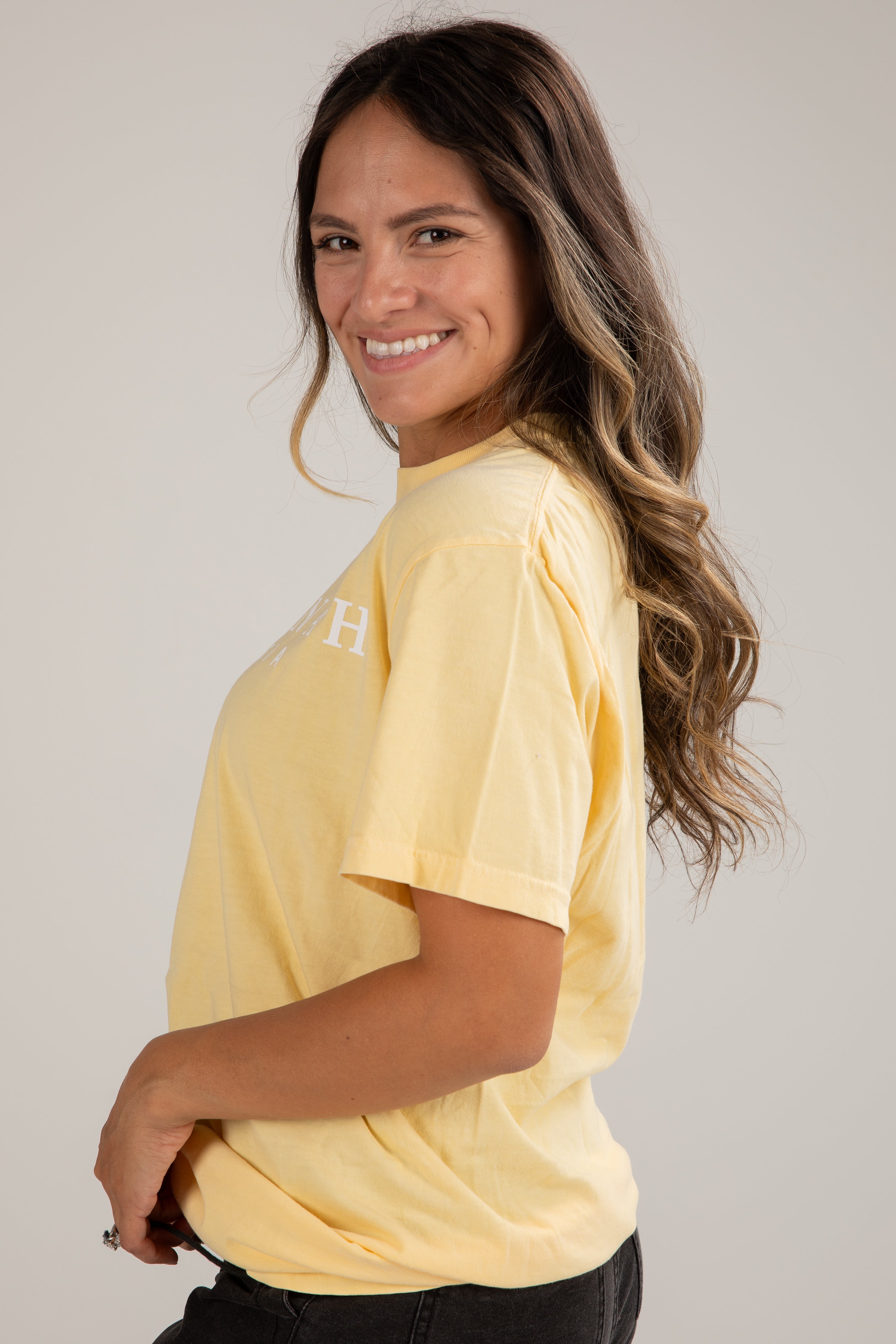Woman wearing a yellow t-shirt with a logo on a plain background