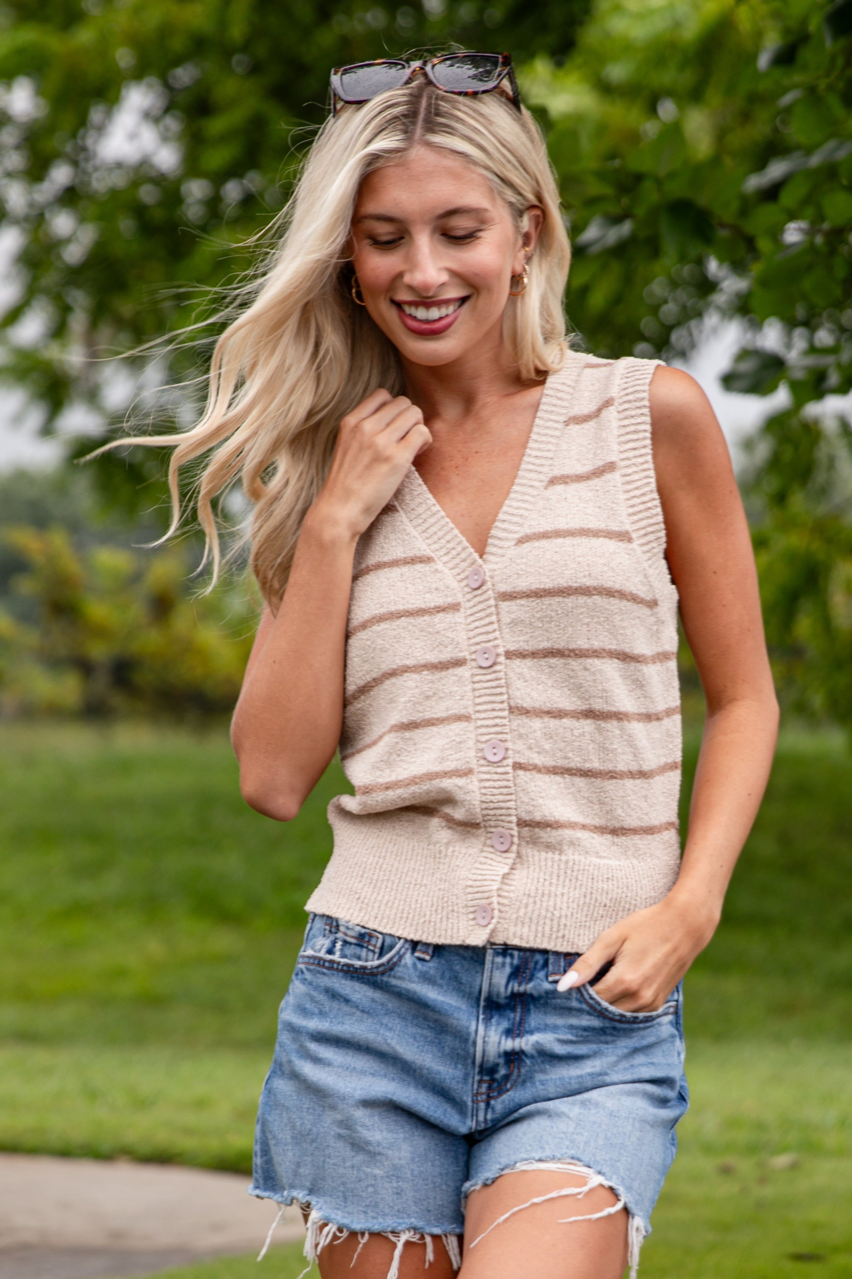 Woman wearing a beige striped sleeveless sweater and denim shorts outdoors.
