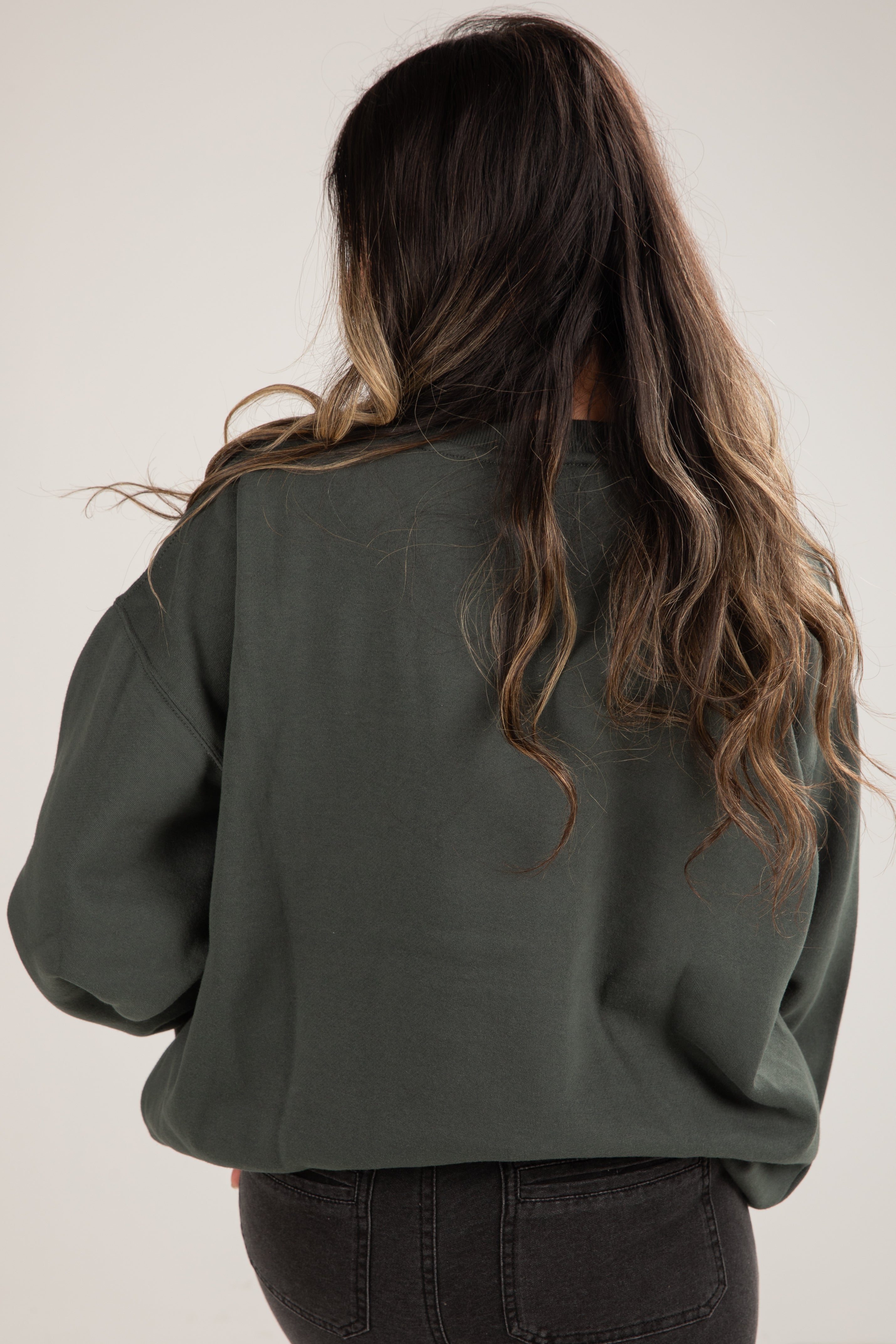 Person wearing a green sweater with long, wavy hair on a plain background