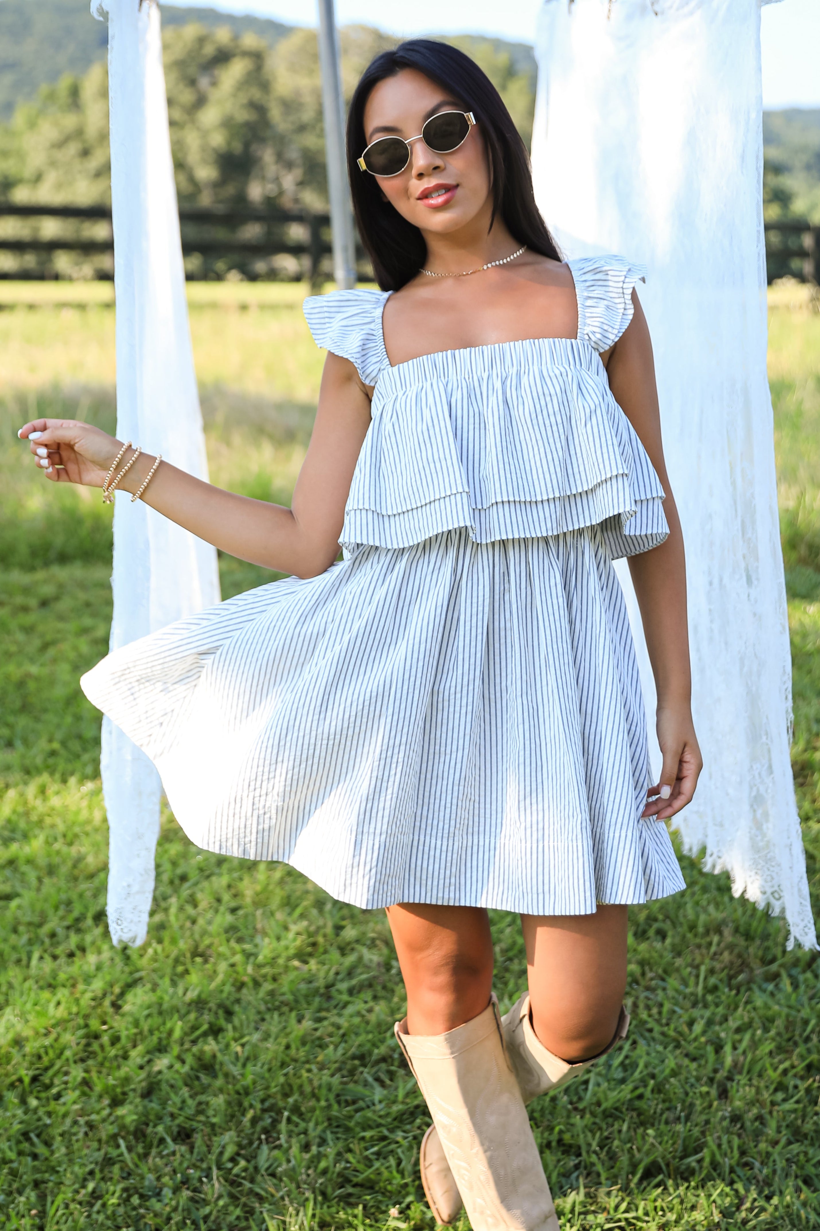 Woman in a blue and white striped dress standing in a grassy field with mountains in the background.