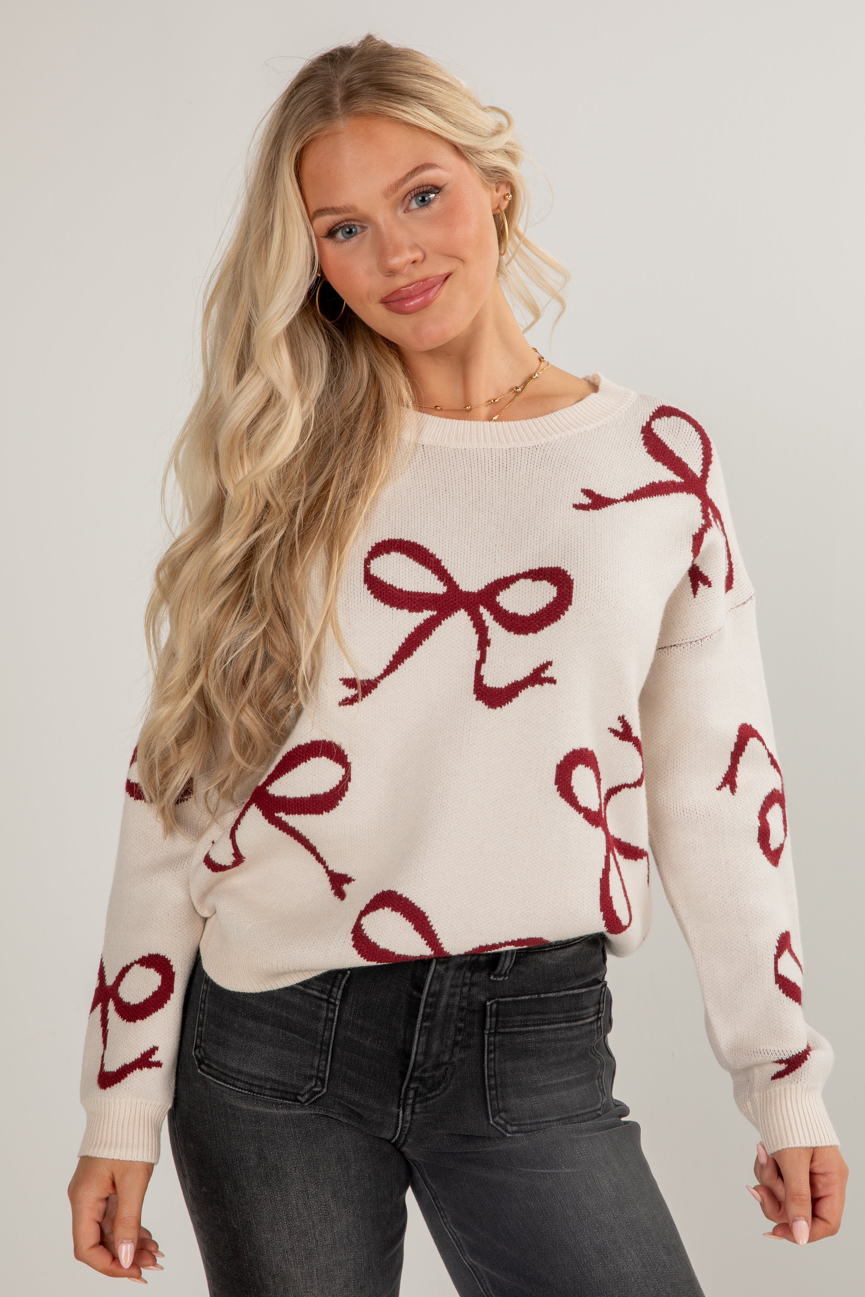 Woman wearing a cream sweater with red bow patterns on a plain background