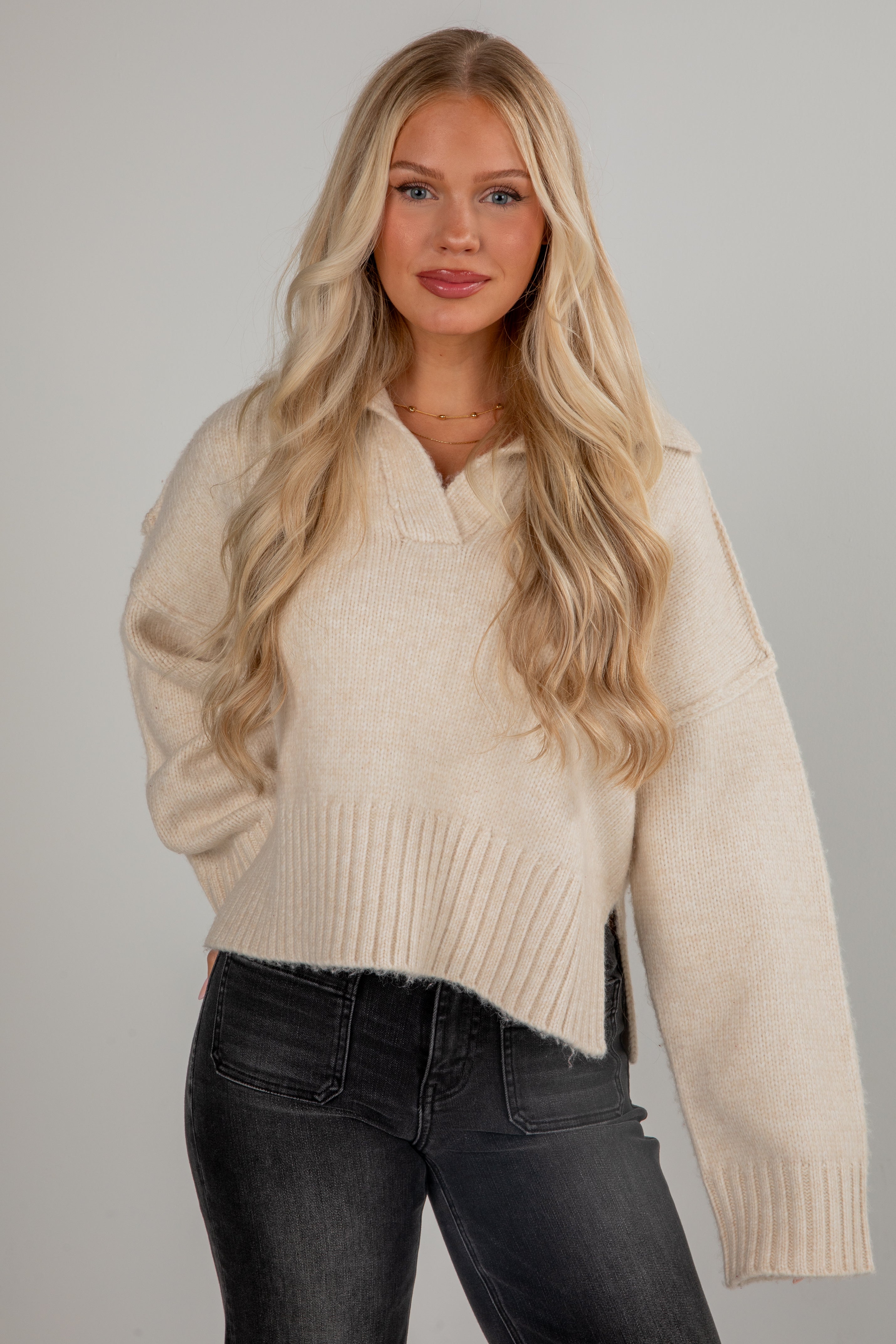 Woman wearing a beige sweater and black pants against a gray background