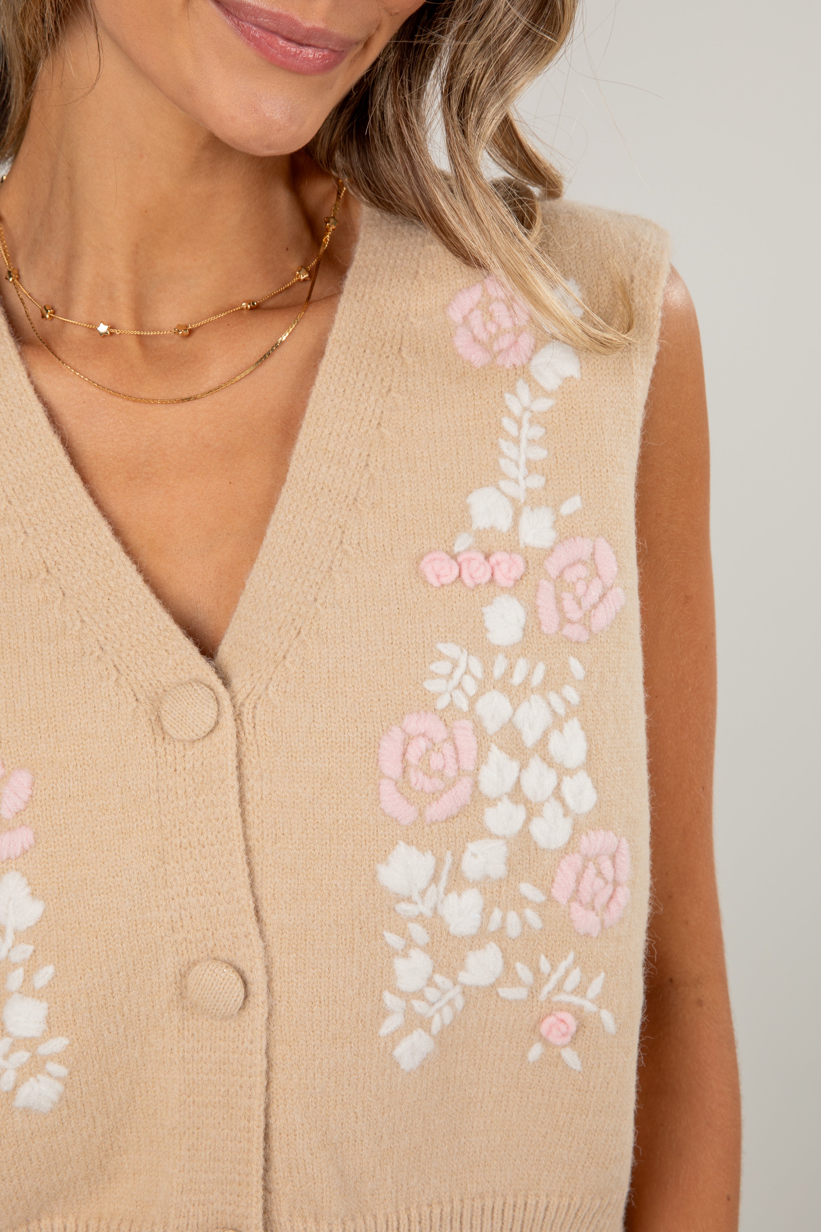 Beige sleeveless sweater vest with floral patterns on a neutral background