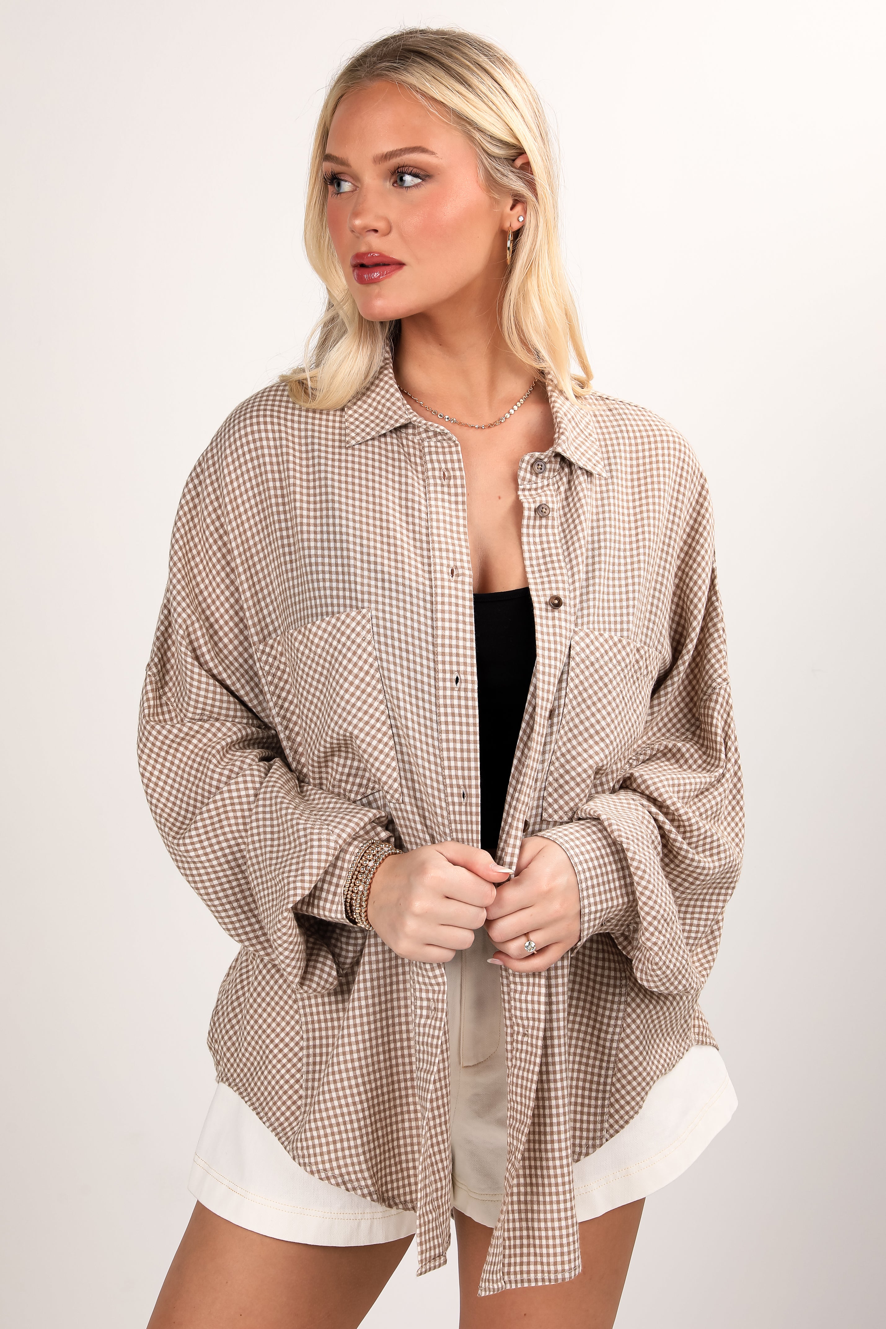 Woman wearing a beige checkered shirt over a black top with white shorts on a plain background