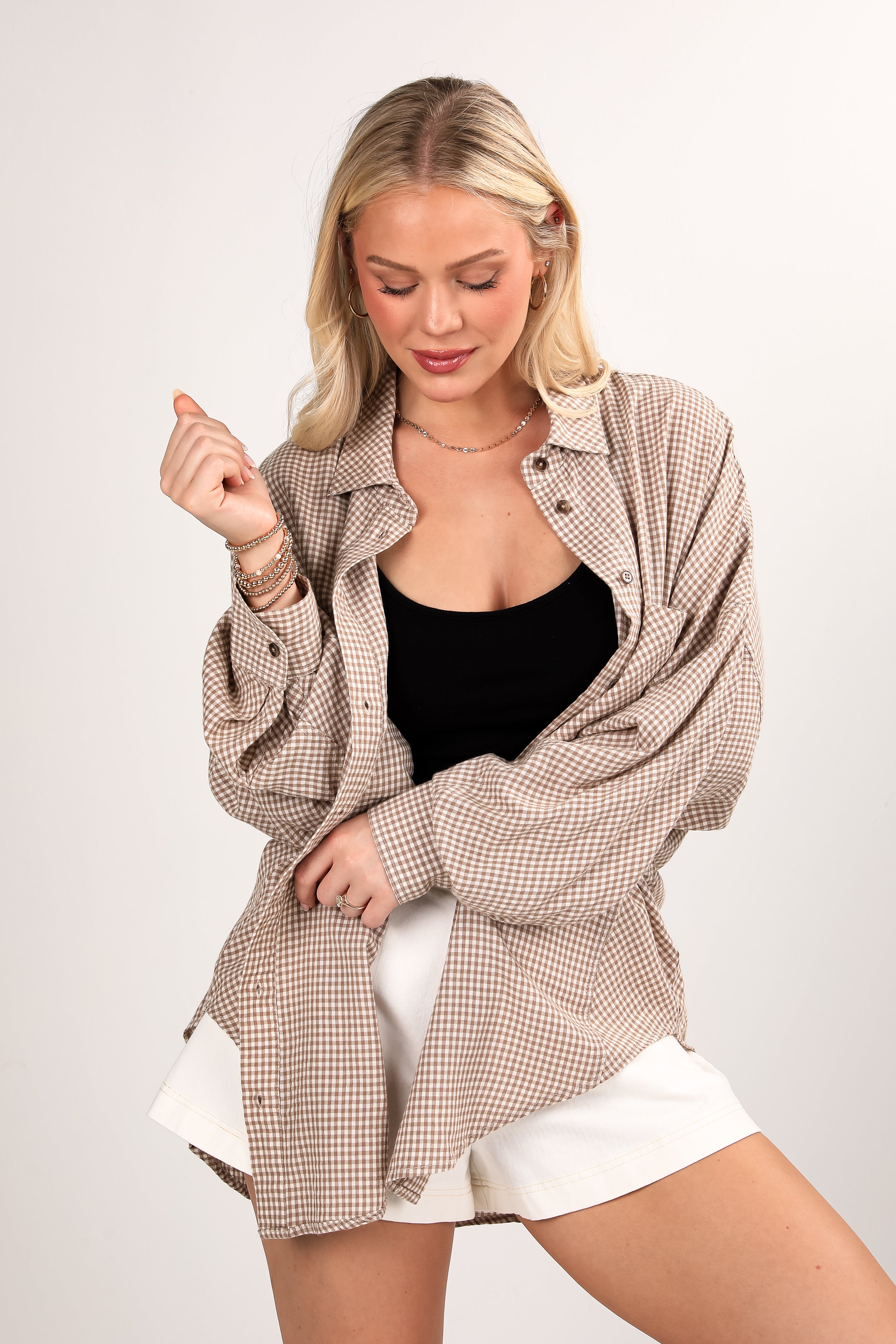 Woman wearing a checkered shirt over a black top and white shorts on a plain background