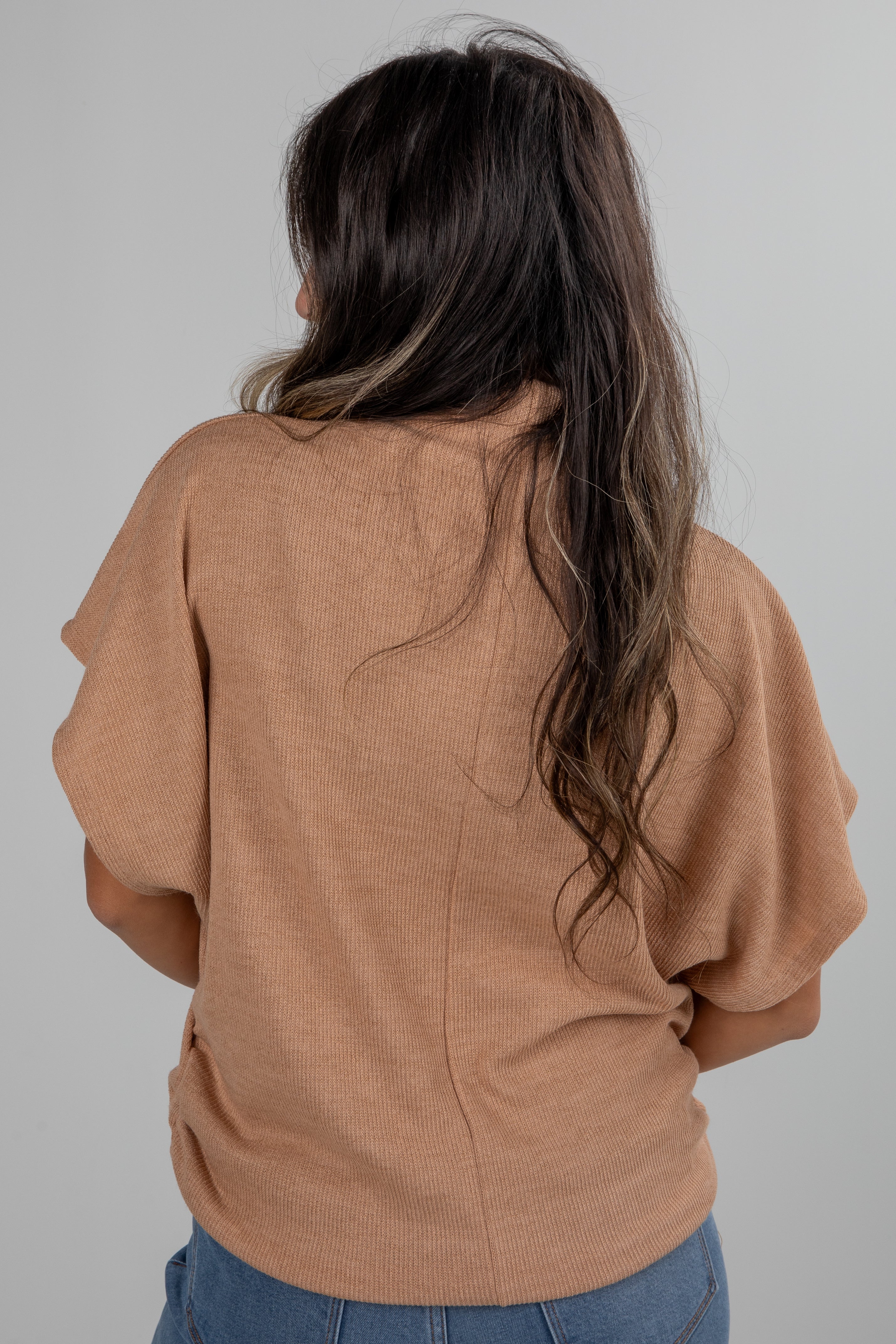 Person wearing a brown sweater with long hair on a plain background