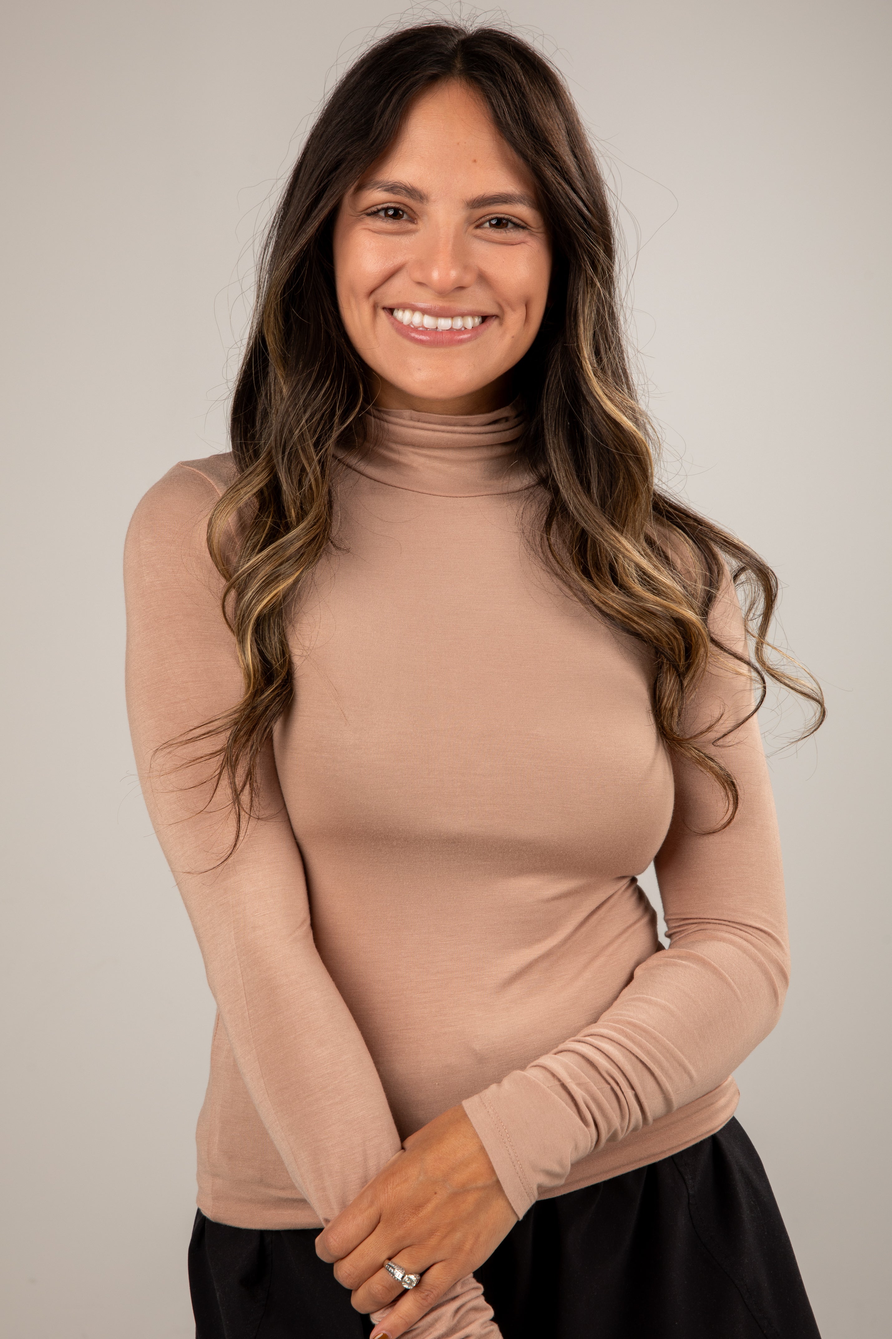 Woman wearing a beige turtleneck sweater against a plain background