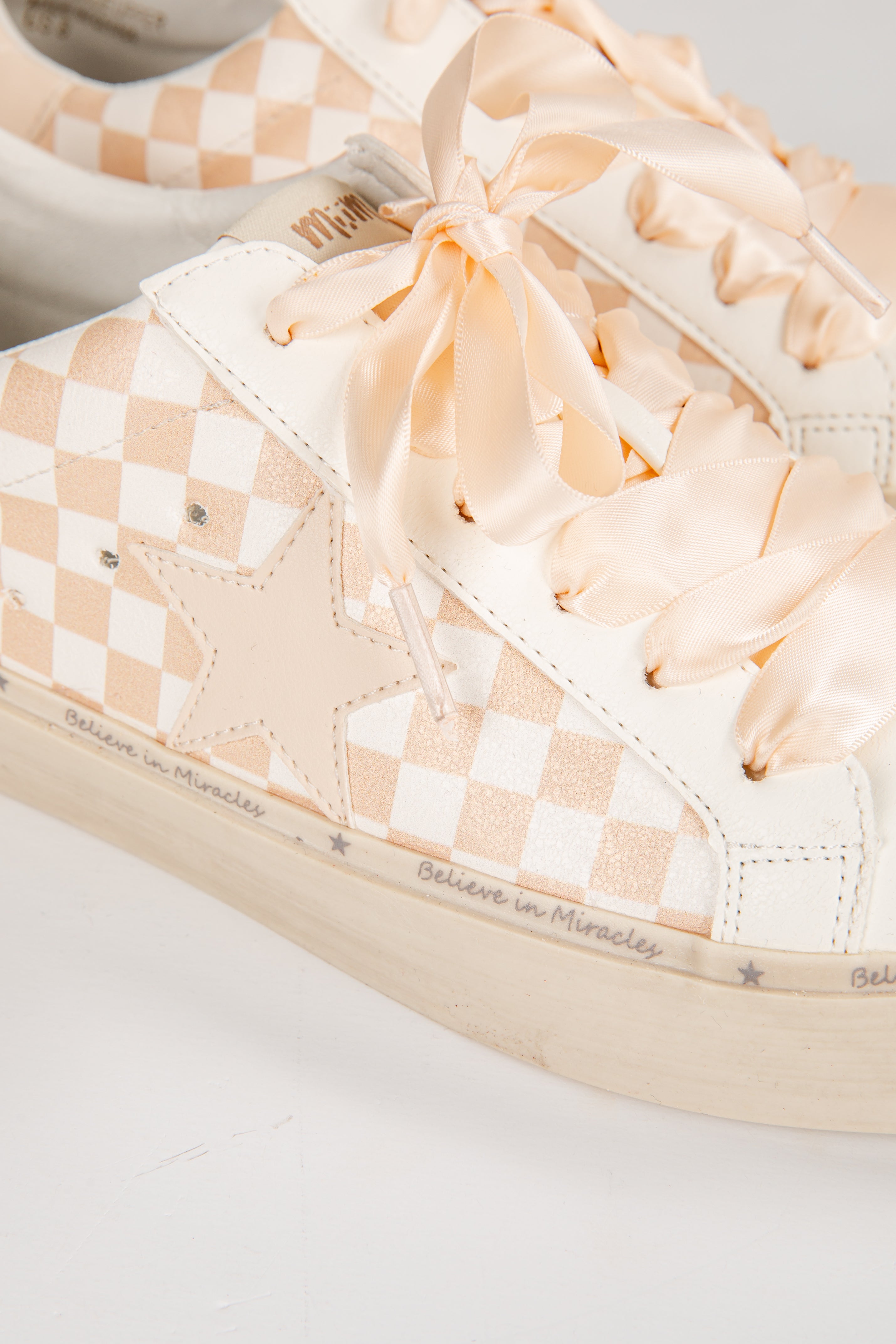 Close-up of a sneaker with checkered pattern and bow detail on a light background