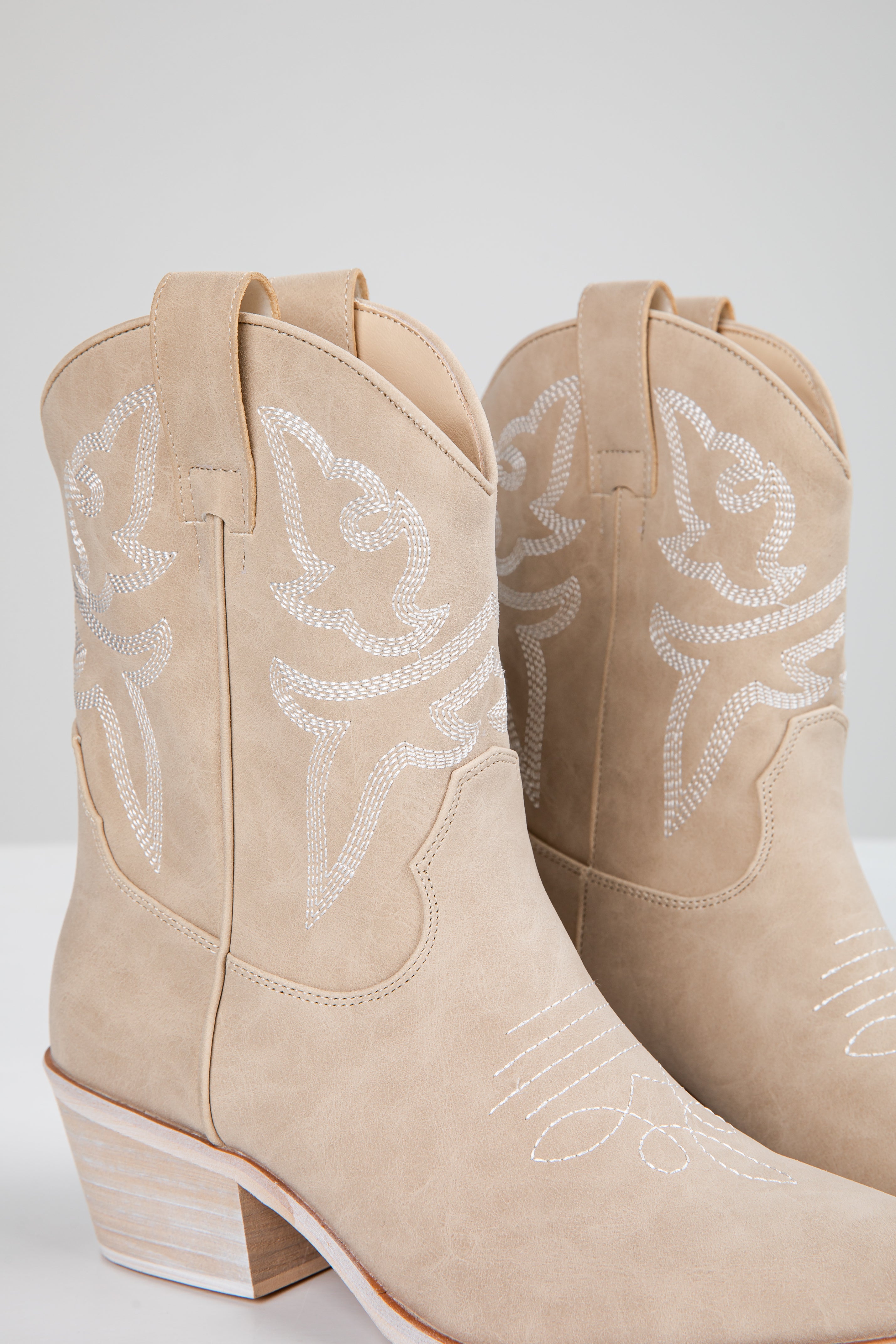 Pair of beige cowboy boots with white embroidery on a light gray background