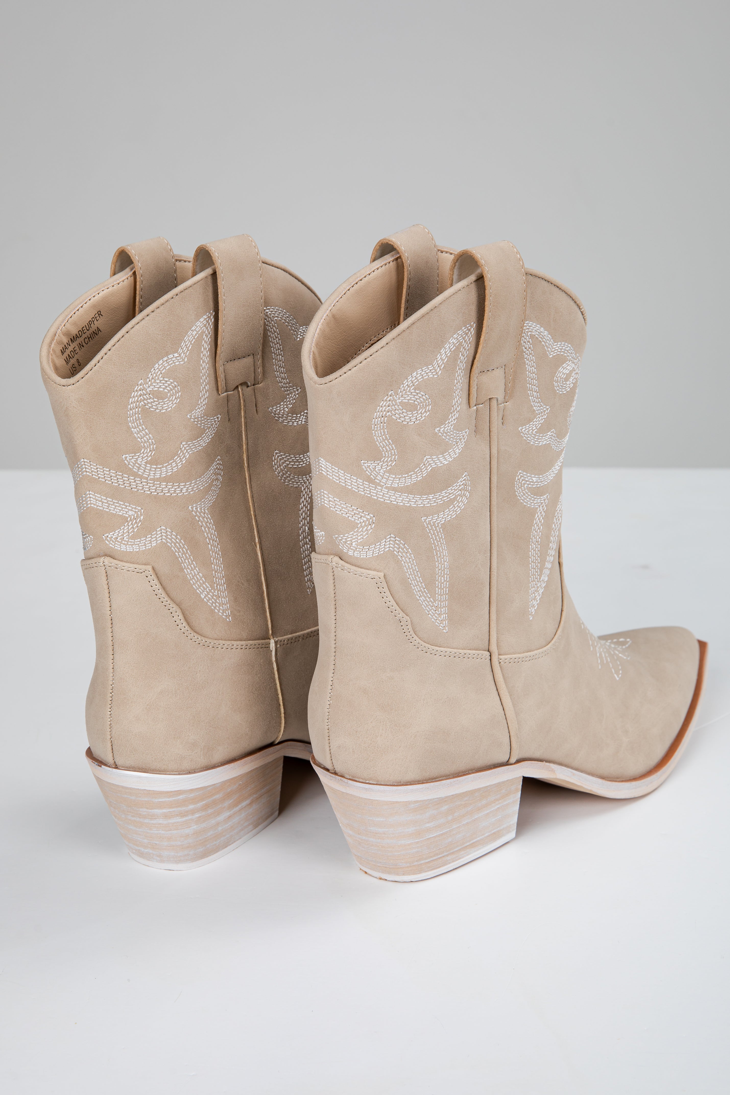 Pair of beige cowboy boots with white star patterns on a light gray background