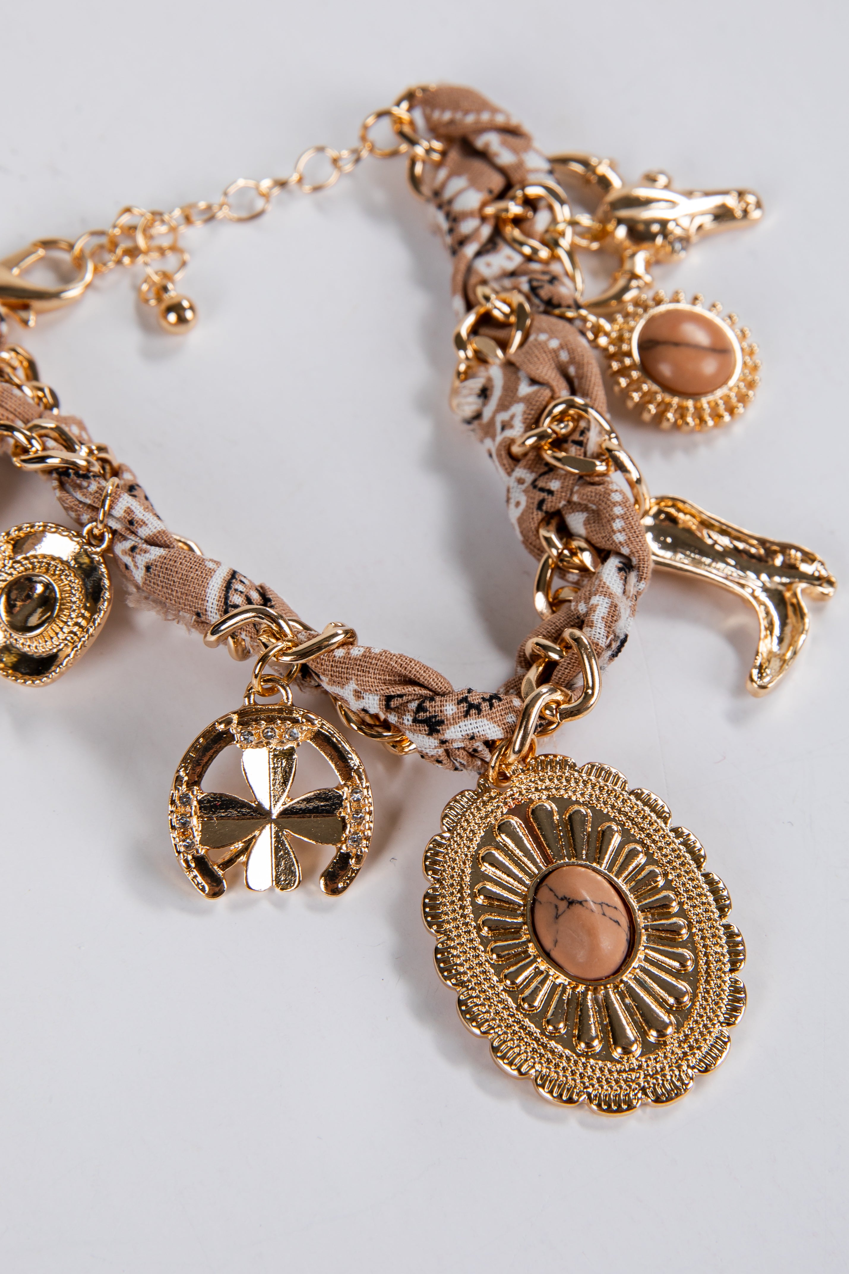 Gold charm bracelet with various charms on a light gray background