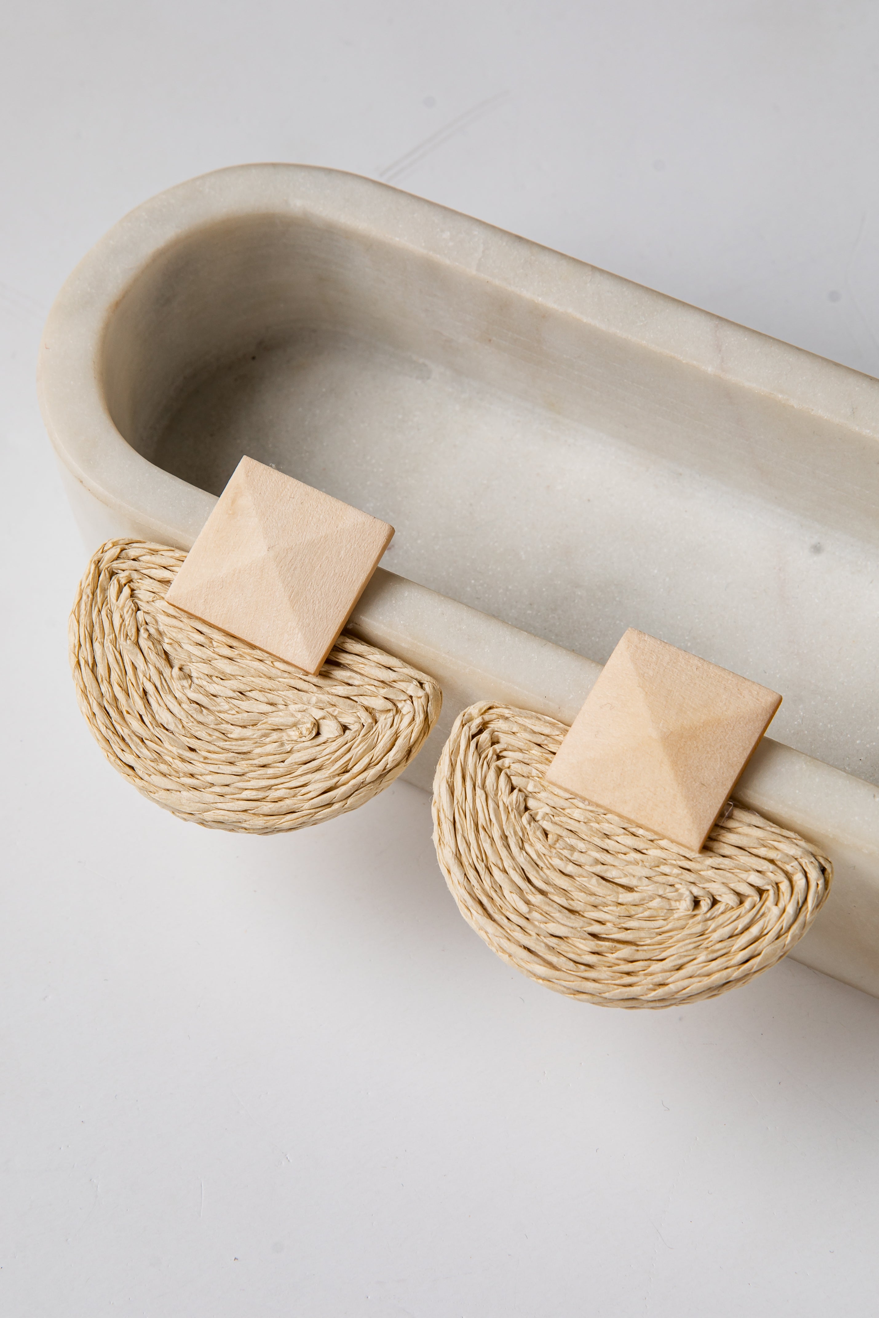 Pair of beige earrings with woven design on a light gray background