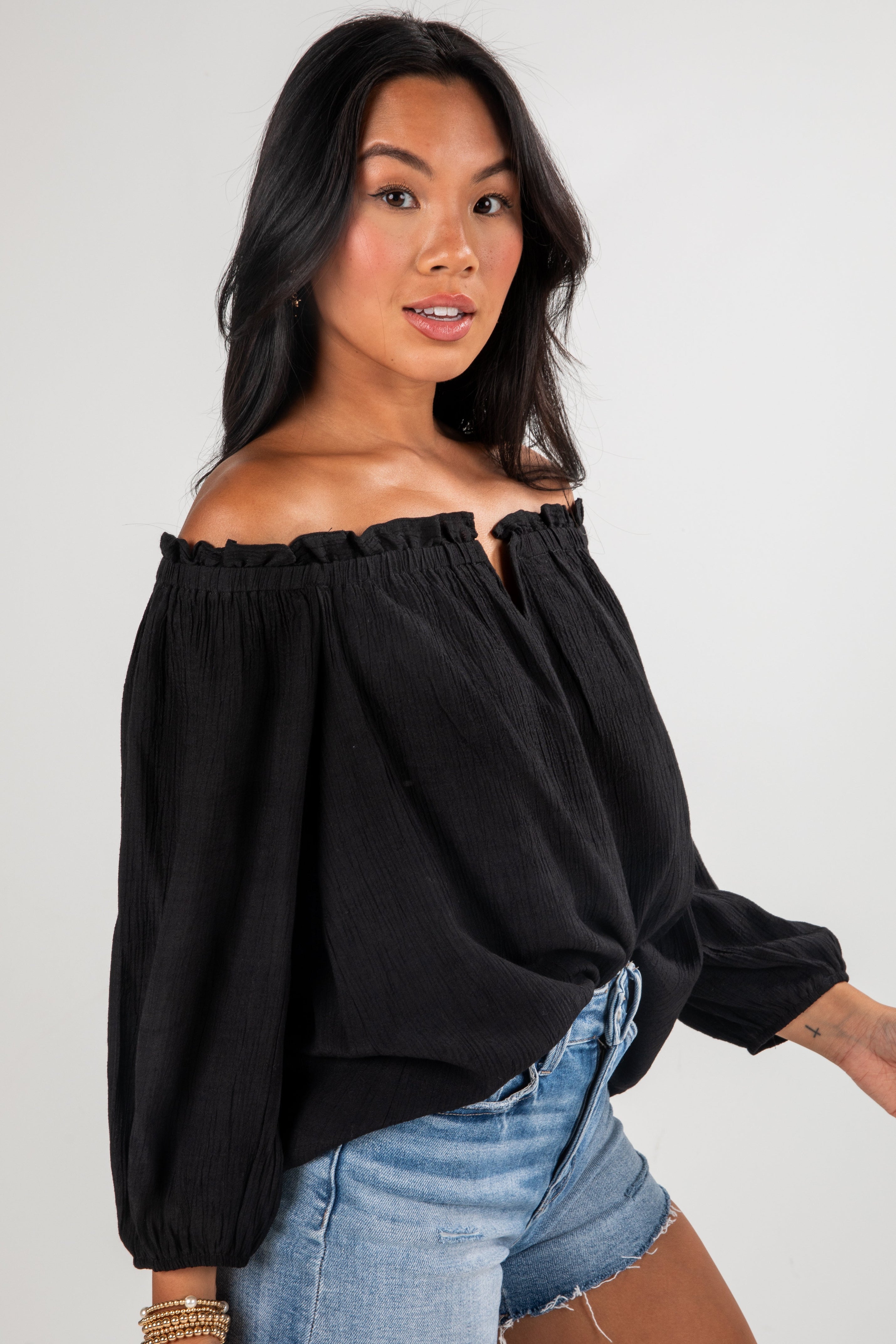 Woman wearing a black off-shoulder top and blue jeans against a plain background