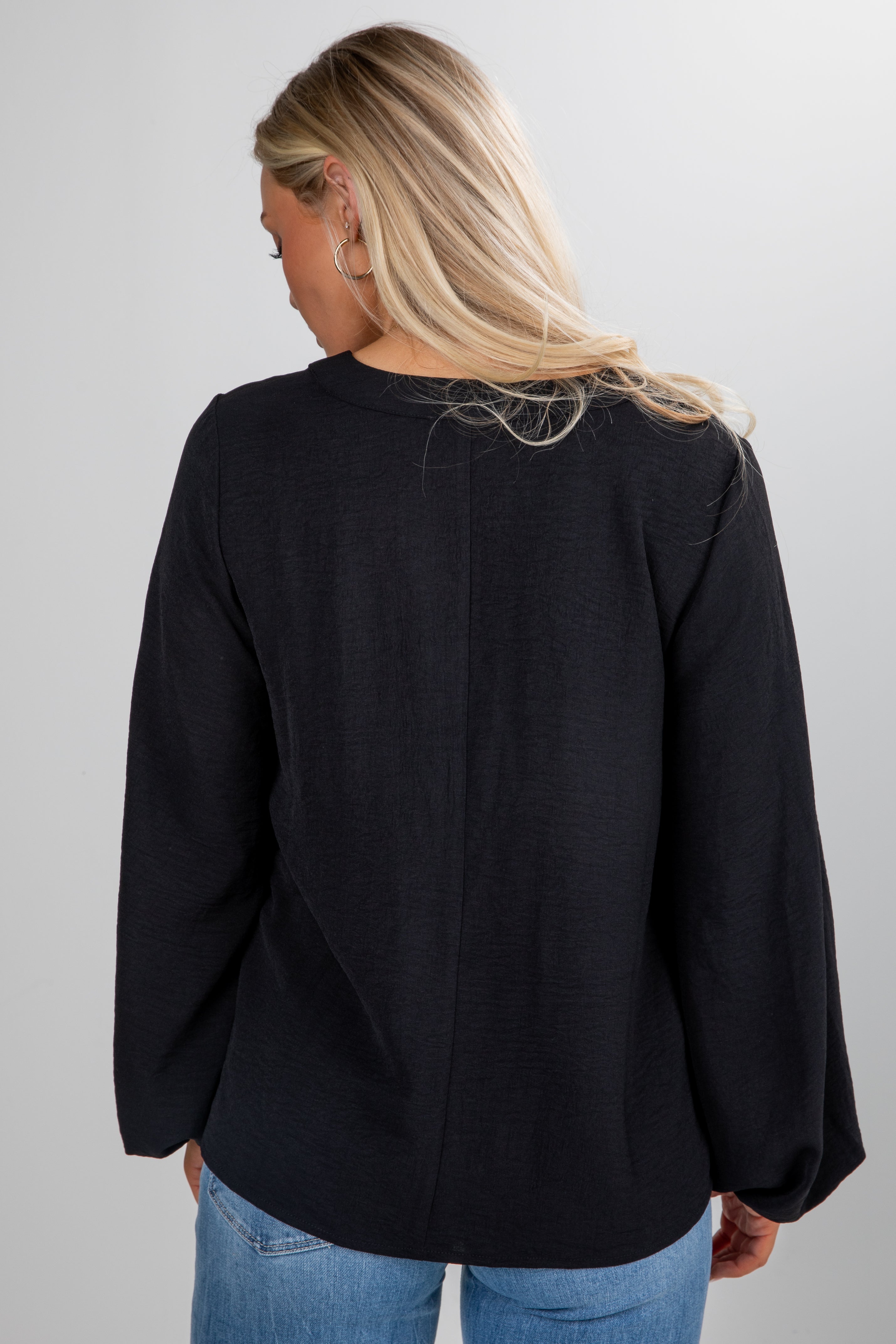 Person wearing a black sweater and blue jeans on a plain background