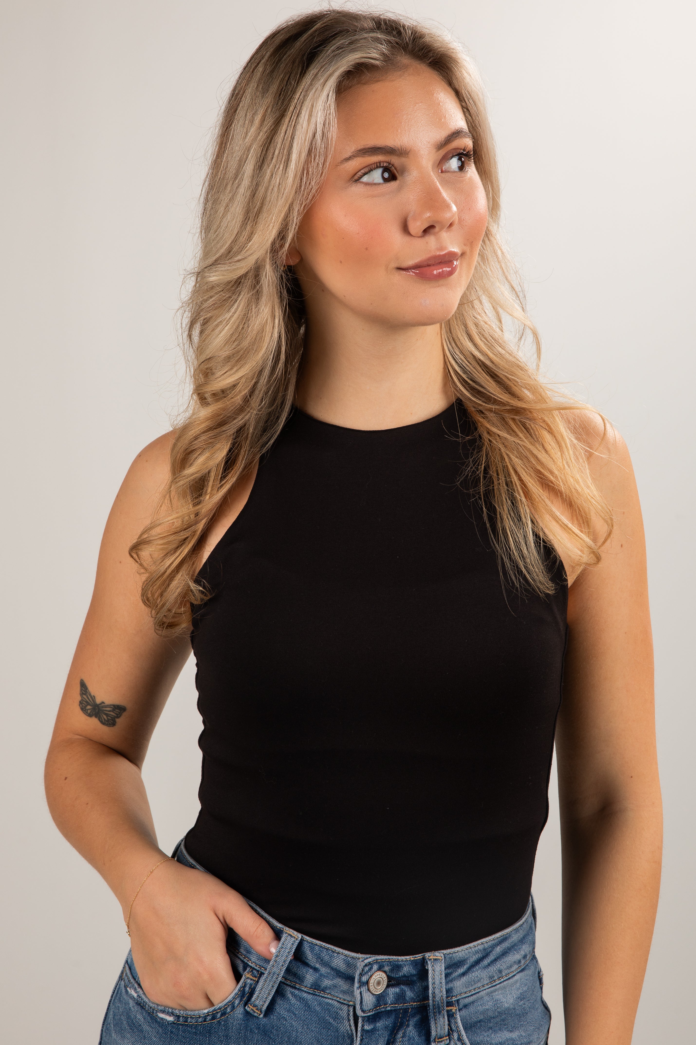 Woman wearing a black sleeveless top and blue jeans against a plain background